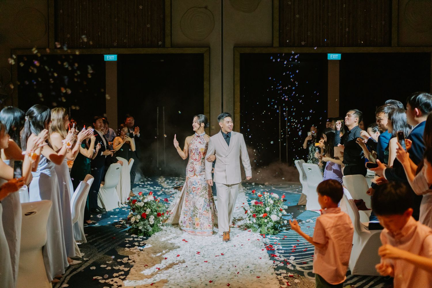 Bride and groom walk down the aisle as guests celebrate with confetti at an elegant indoor wedding reception.