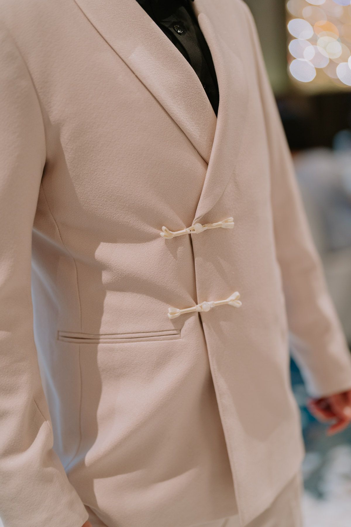 Close-up of a cream blazer with decorative bow closures and black shirt underneath at a formal event.
