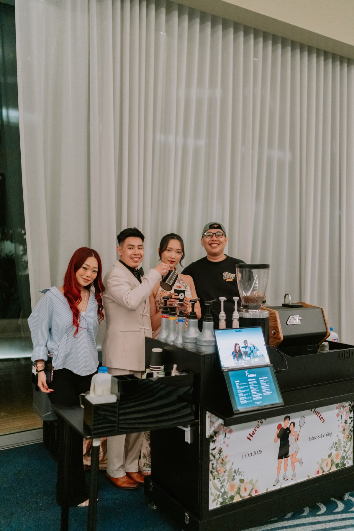 Four people posing together behind a coffee cart station at an indoor event venue.