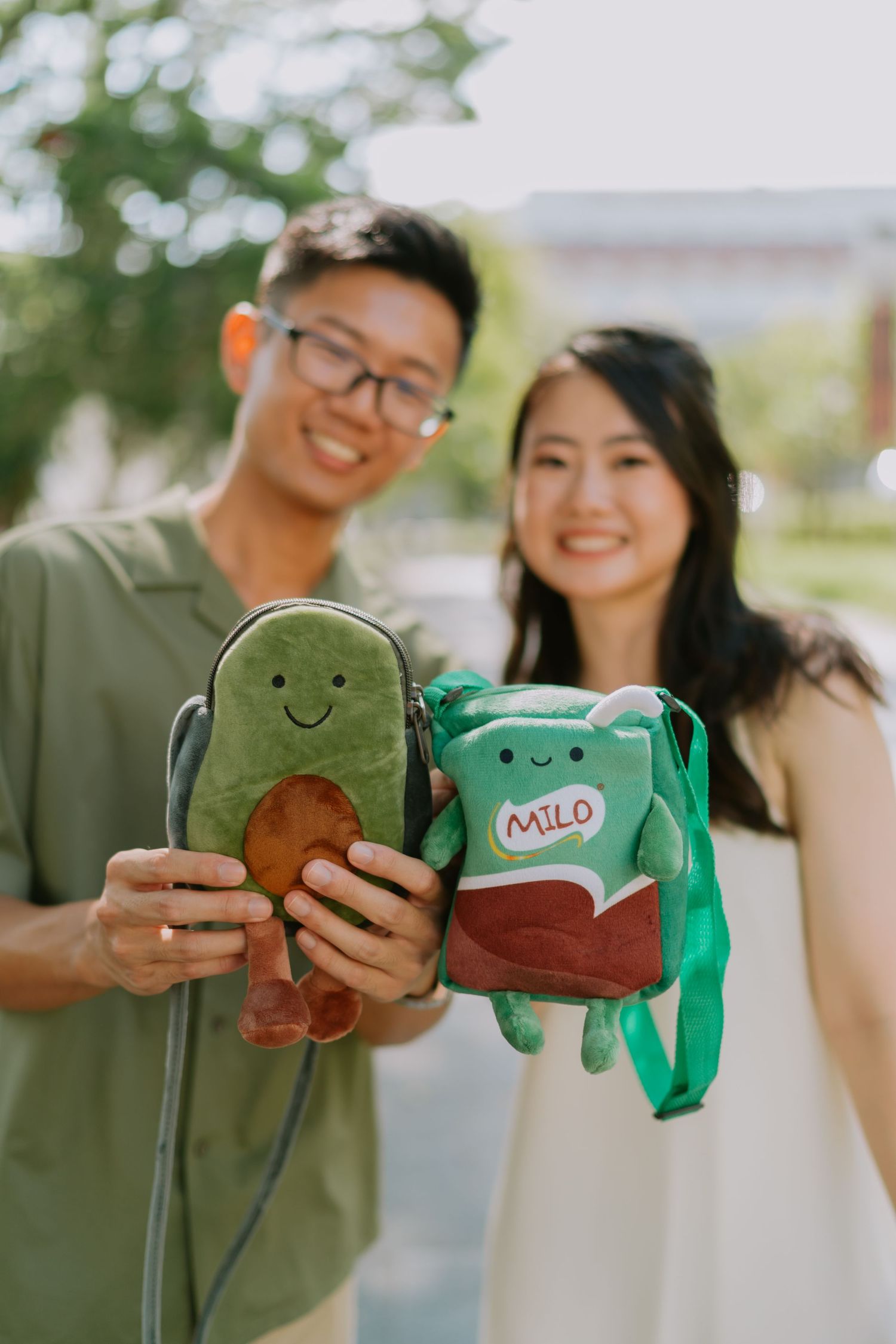 Smiling couple holding cute avocado and Milo plush bag charms outdoors.