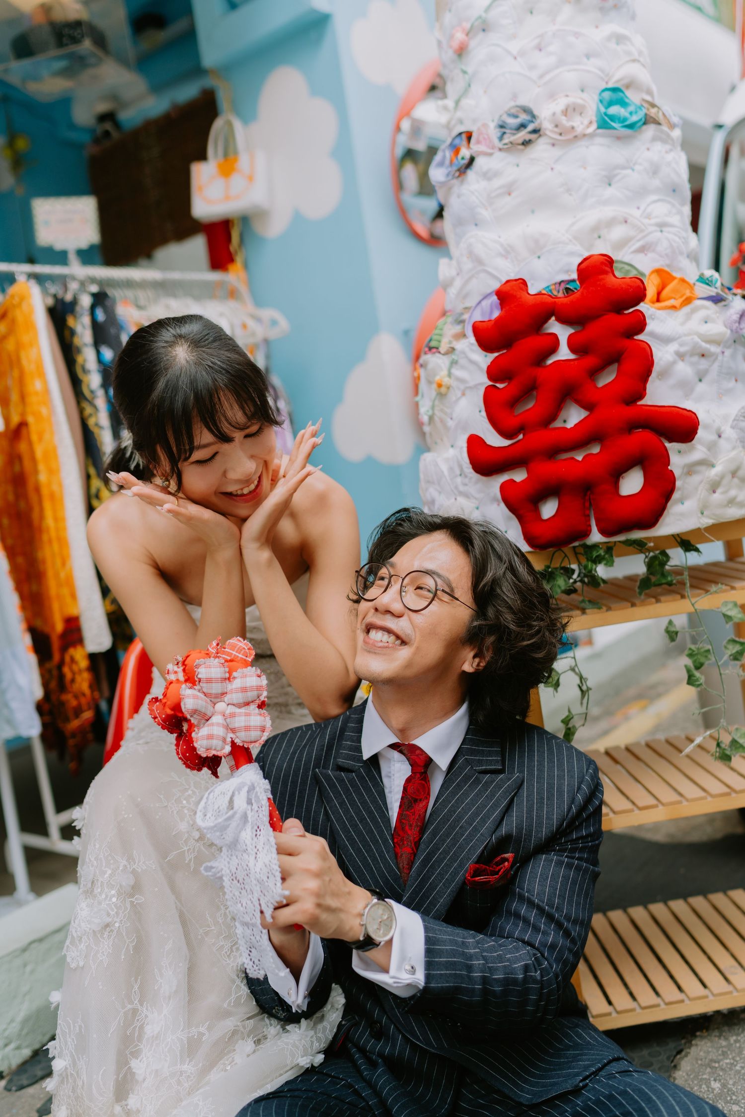 Bride and groom sharing a tender moment beside a double happiness wedding cake sculpture outside a vintage shop.