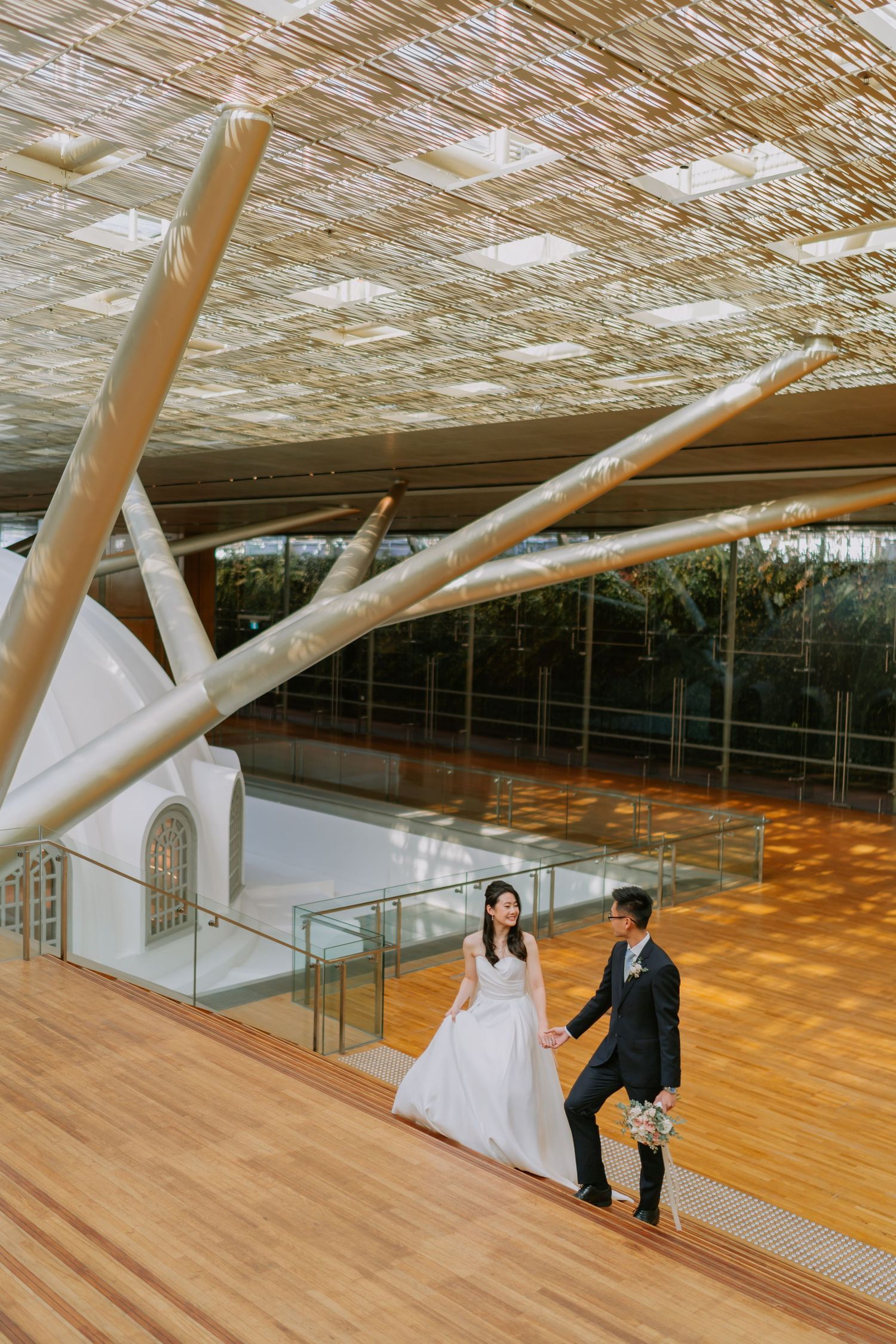 Couple walking hand in hand on a wooden floor under a dramatic branching ceiling structure.