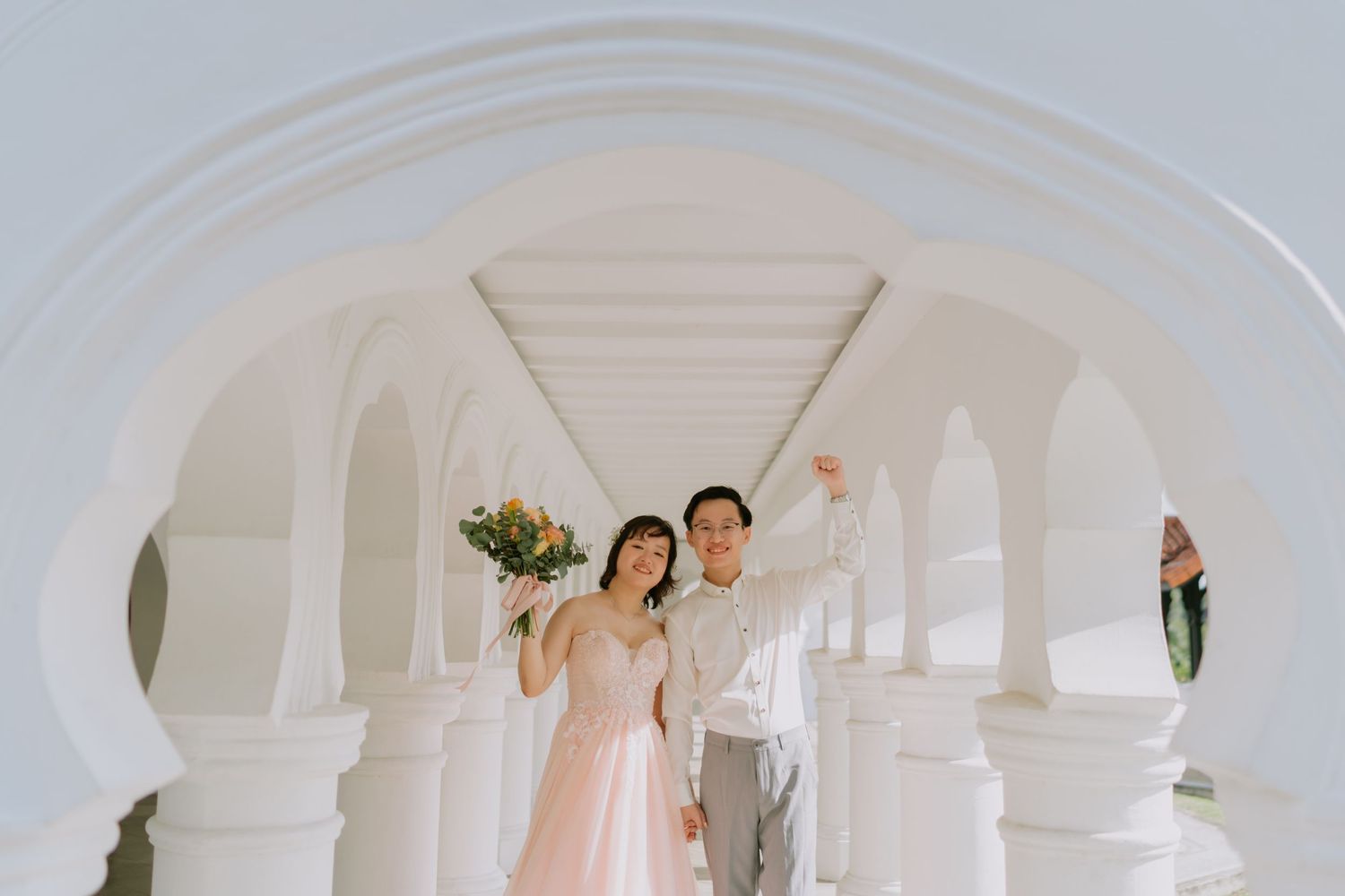 Joyful bride and groom celebrating under white arches, groom raising his fist in excitement.