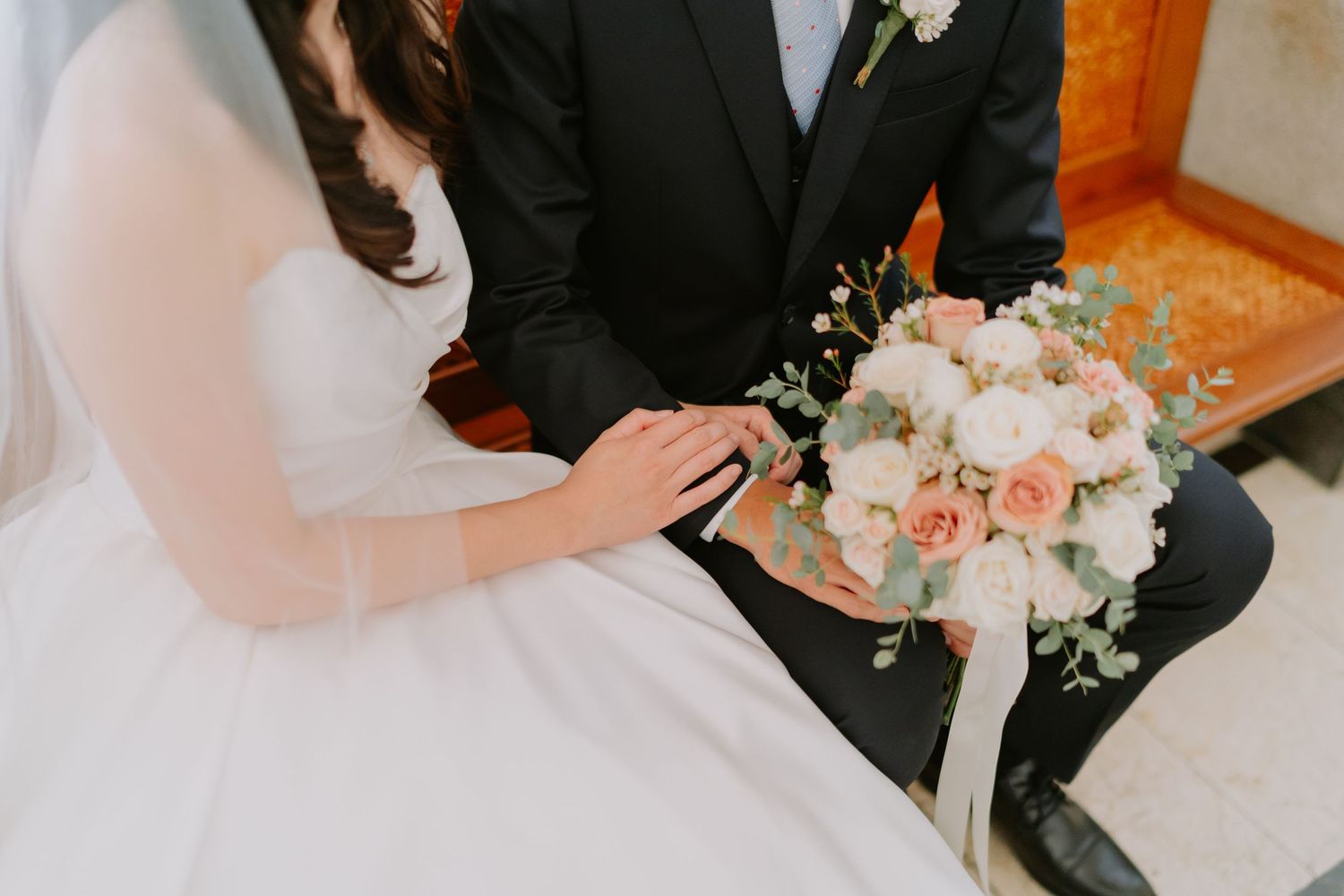 Close-up of bride and groom holding hands with elegant pink and white floral wedding bouquet with eucalyptus.