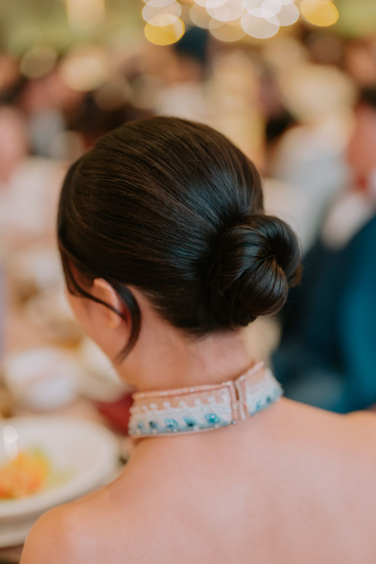 Elegant low bun hairstyle on a woman at a formal event, showcasing sleek dark hair and decorative neckline.