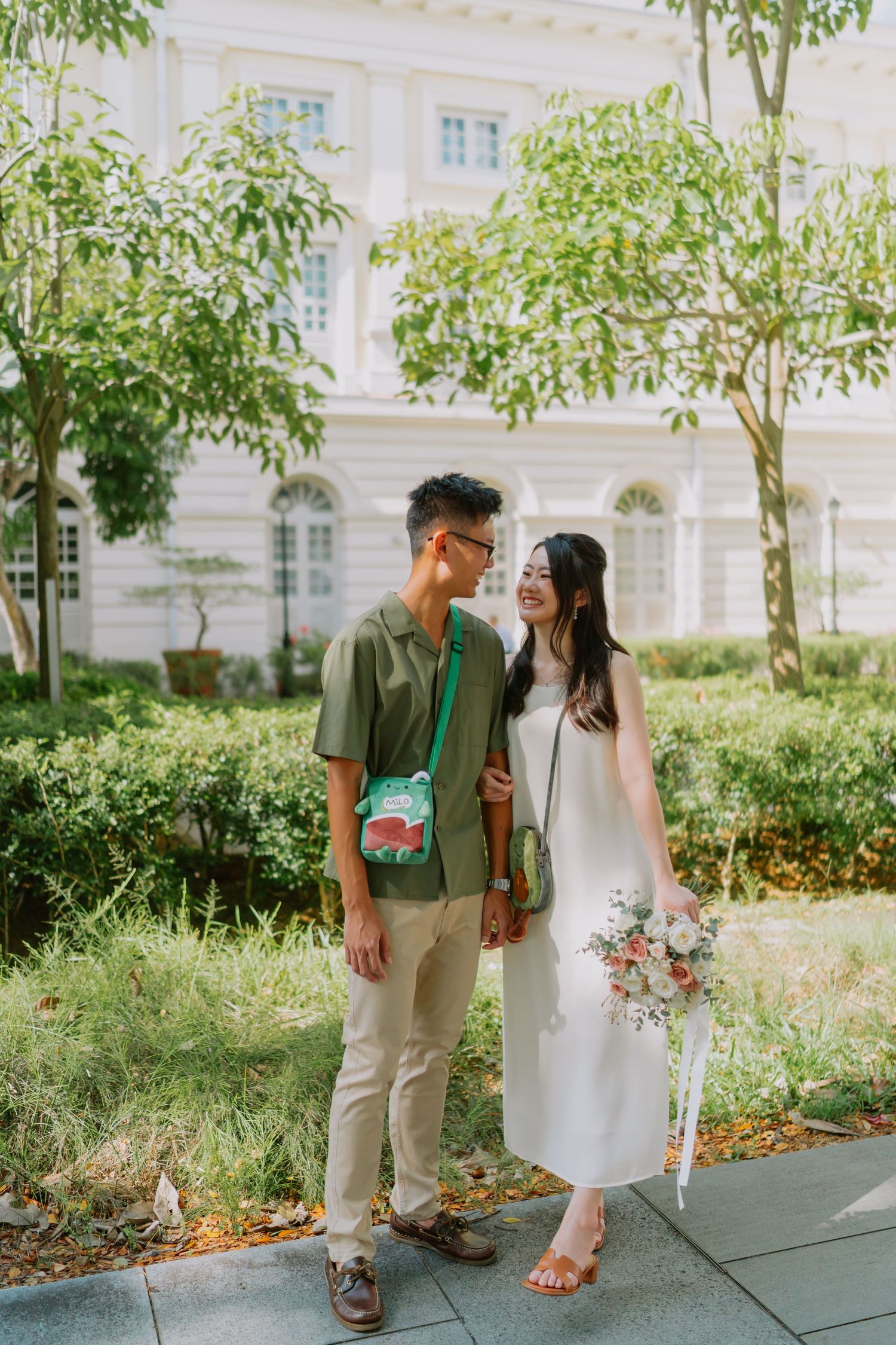 Couple standing close together smiling in a lush green garden setting.