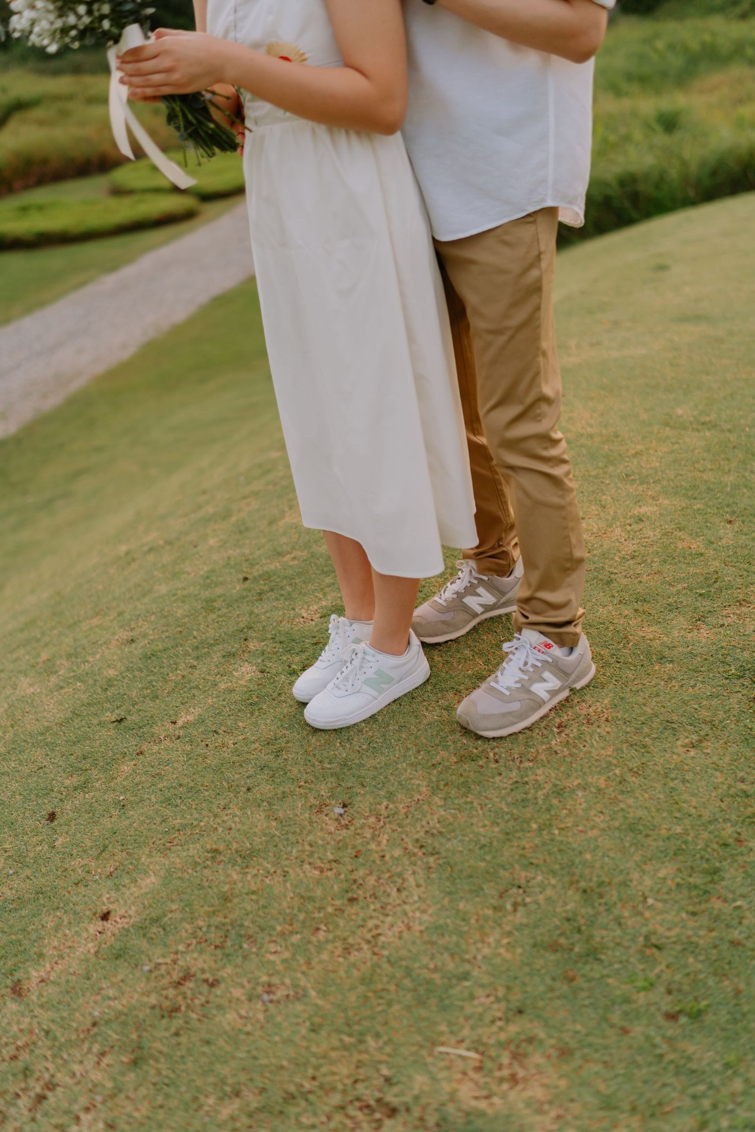 Close-up of a couple standing on grass wearing New Balance sneakers, the woman in a white dress.