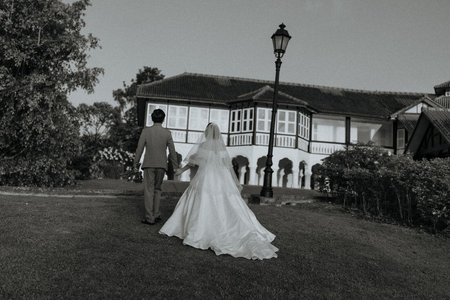 Black and white photo of newlyweds walking hand in hand toward a colonial-style venue building.