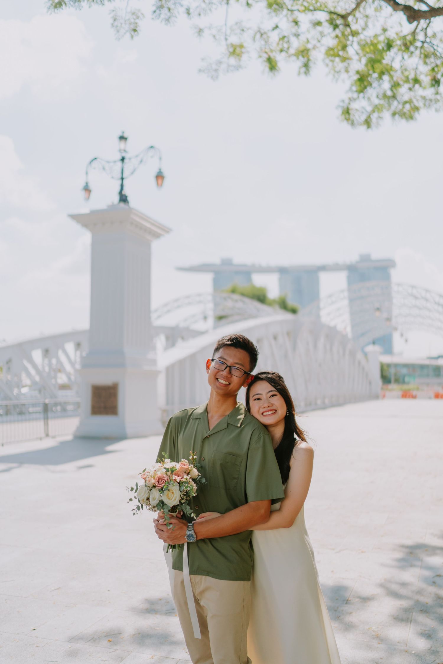 Couple embracing with bouquet near Anderson Bridge and Marina Bay Sands.