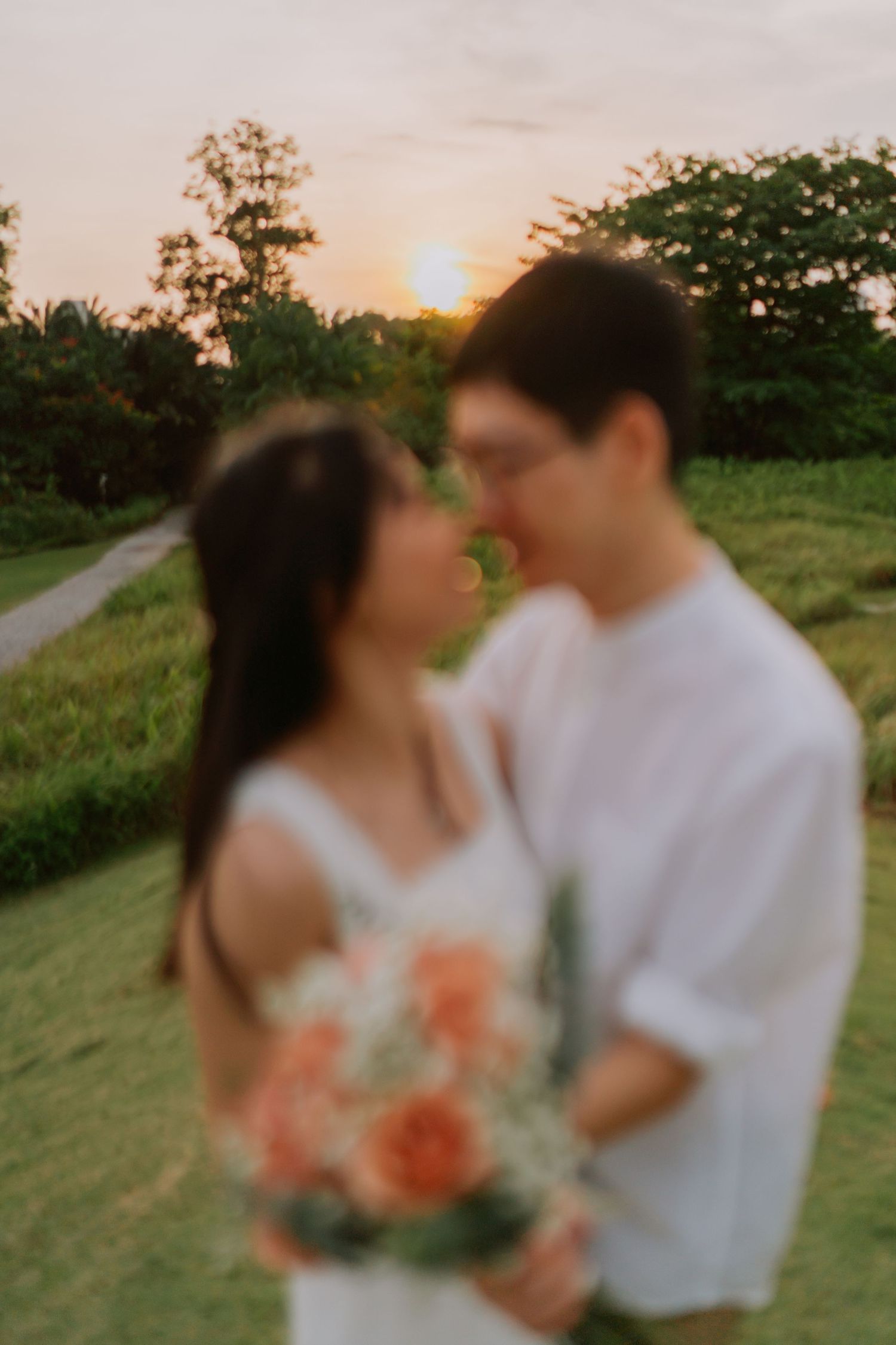 A blurred romantic shot of a couple nearly kissing at sunset, the woman holding an orange bouquet.