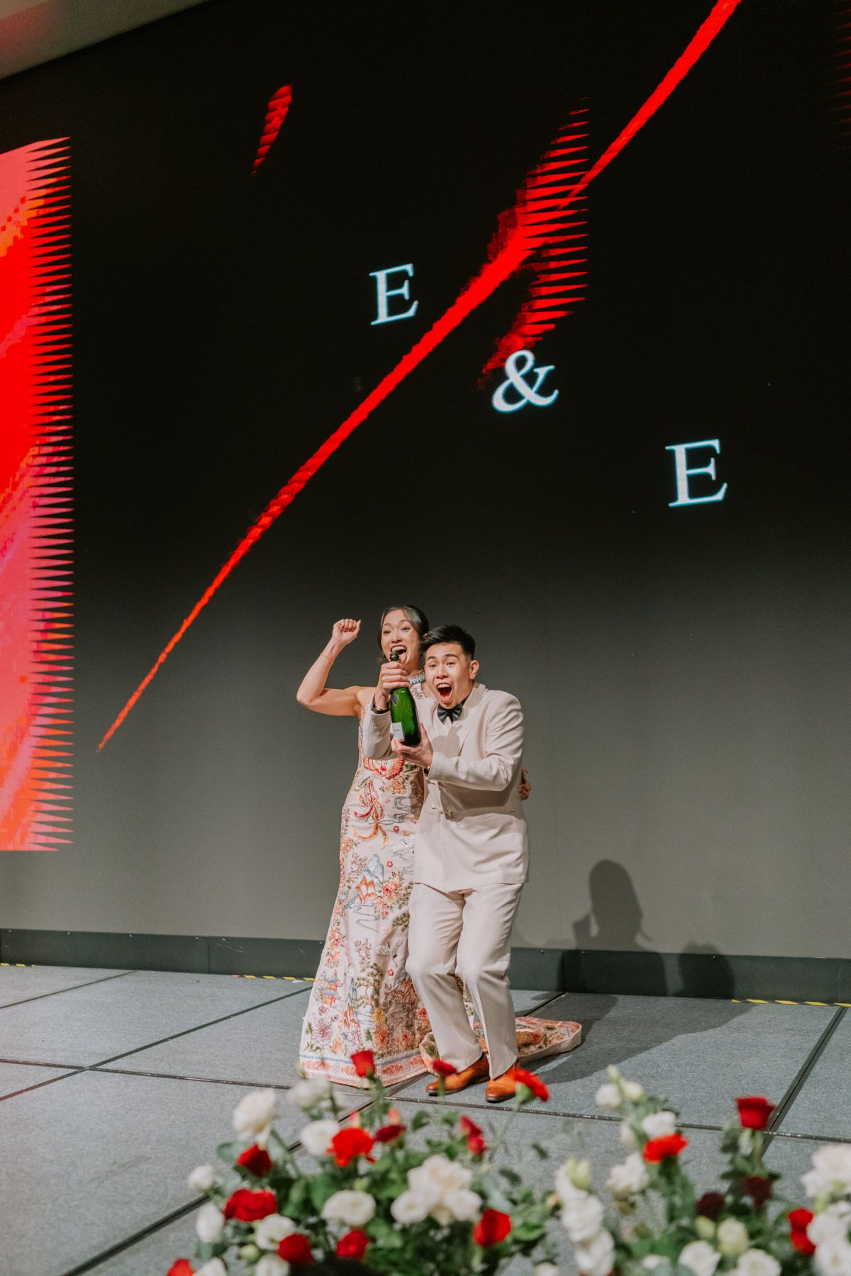 Joyful newlyweds celebrate with champagne in front of an E&E monogram projection at their wedding reception.