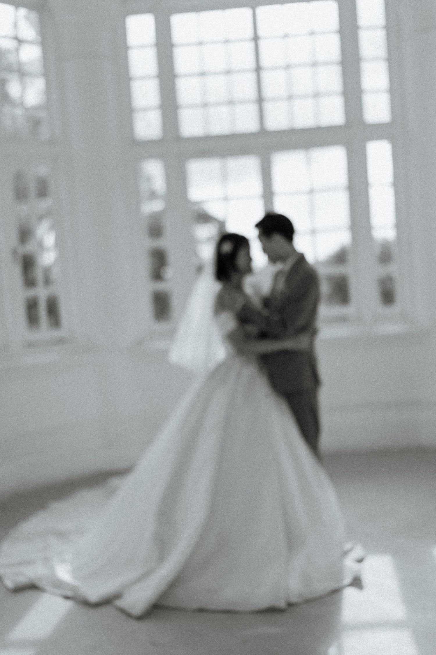 Blurred black and white photo of bride and groom sharing an intimate moment in a bright white room.