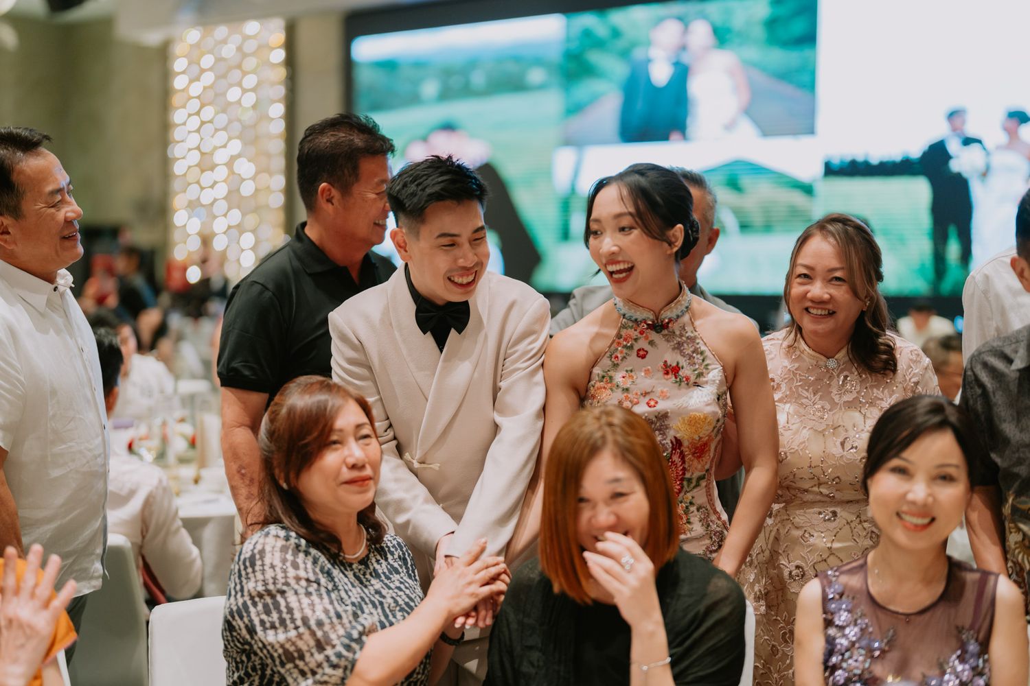Joyful wedding reception with couple in formal attire smiling among guests at elegant banquet hall.