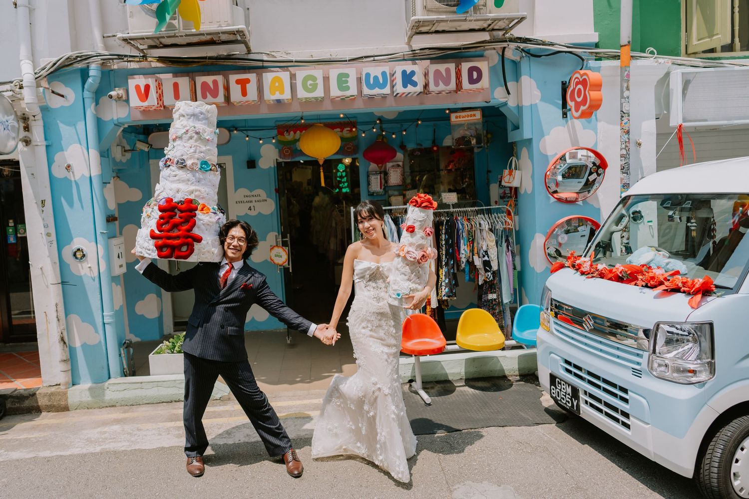 Joyful bride and groom holding hands outside Vintage WKND shop with festive wedding decorations and a white van.