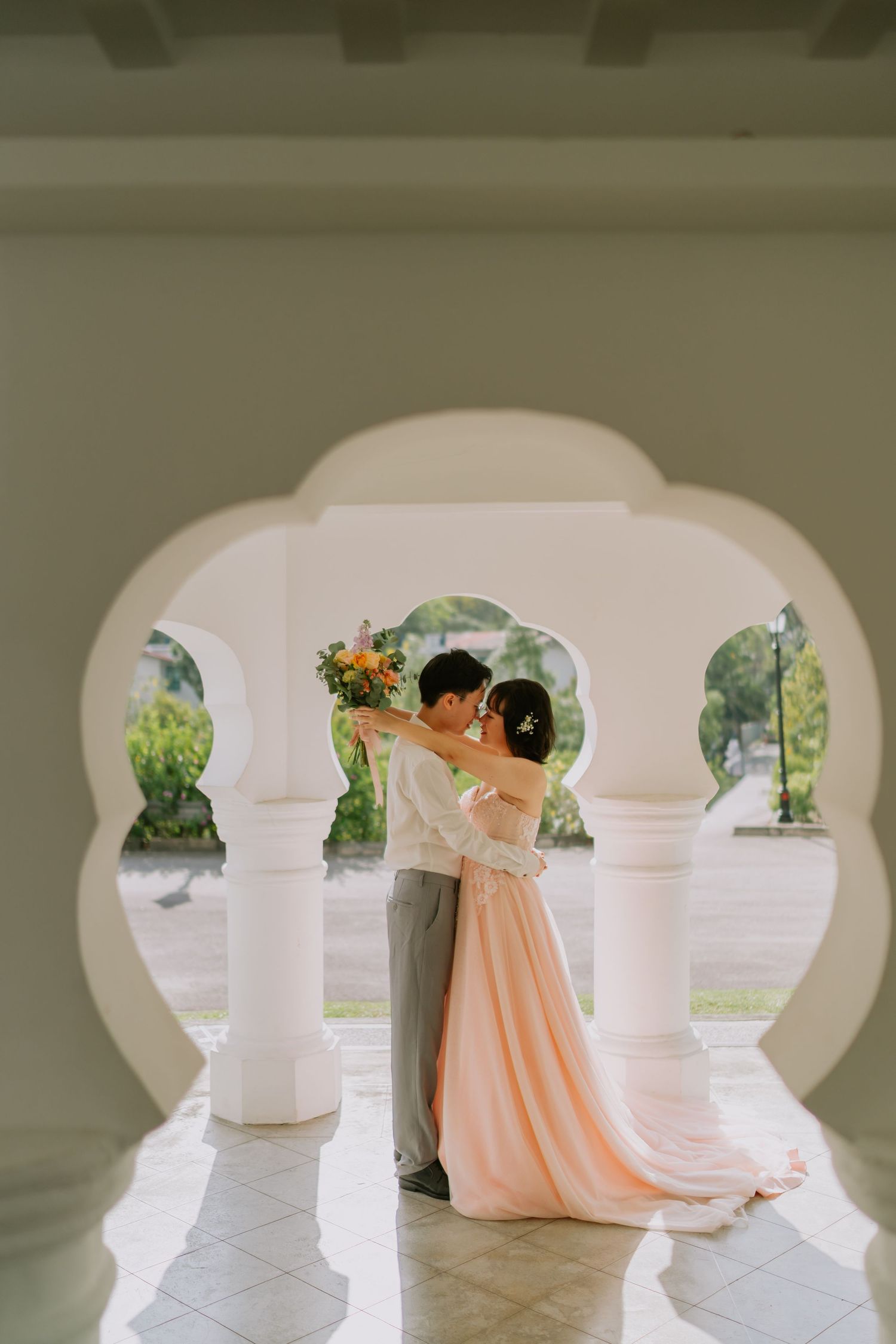 Bride and groom sharing a romantic kiss under ornate white Moorish arches with colorful bouquet.