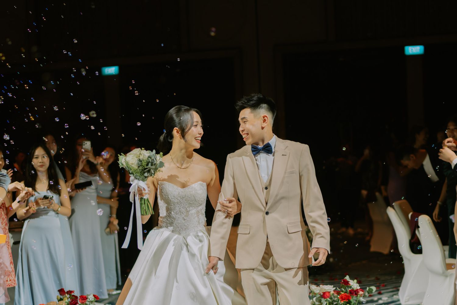 Bride and groom walk down the aisle smiling, surrounded by guests in a elegant wedding venue with confetti.