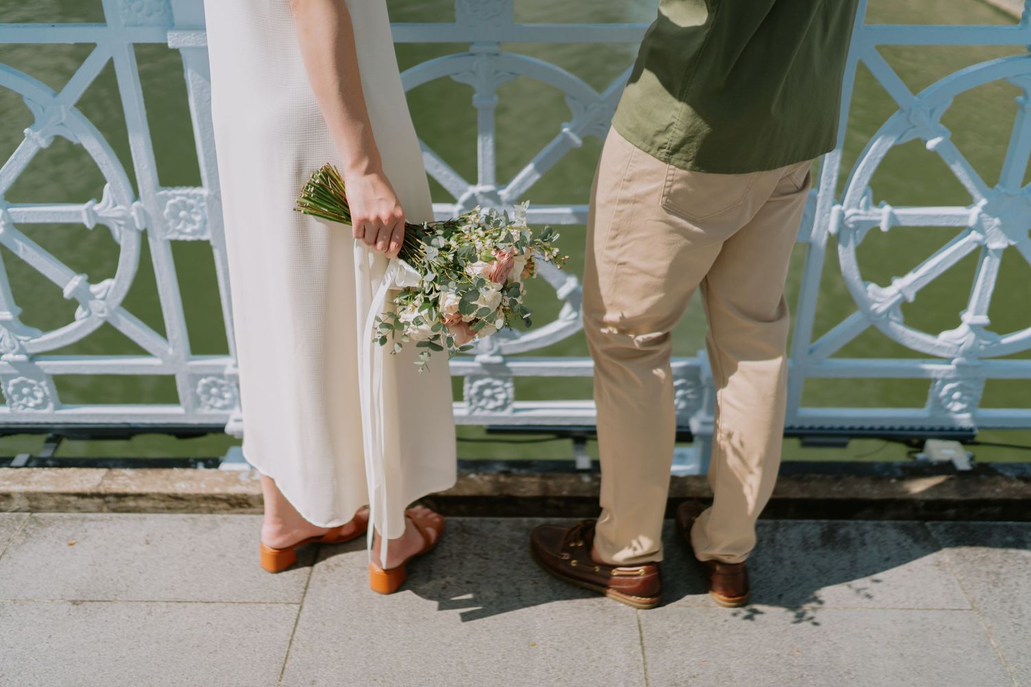 Close-up of couple standing on bridge, woman holding a wildflower bouquet.