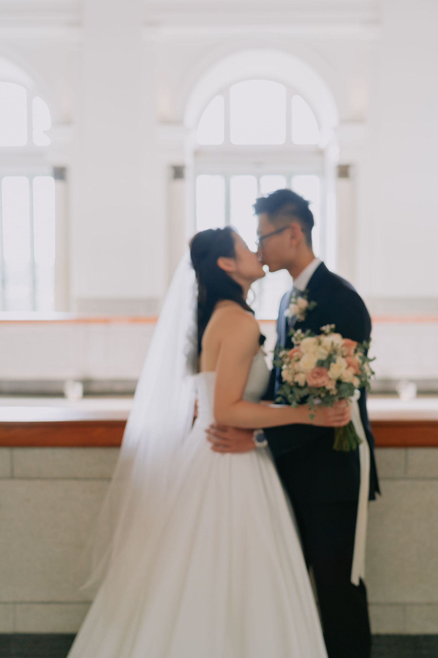 Bride and groom sharing a tender kiss, bride holding pink and white floral bouquet.