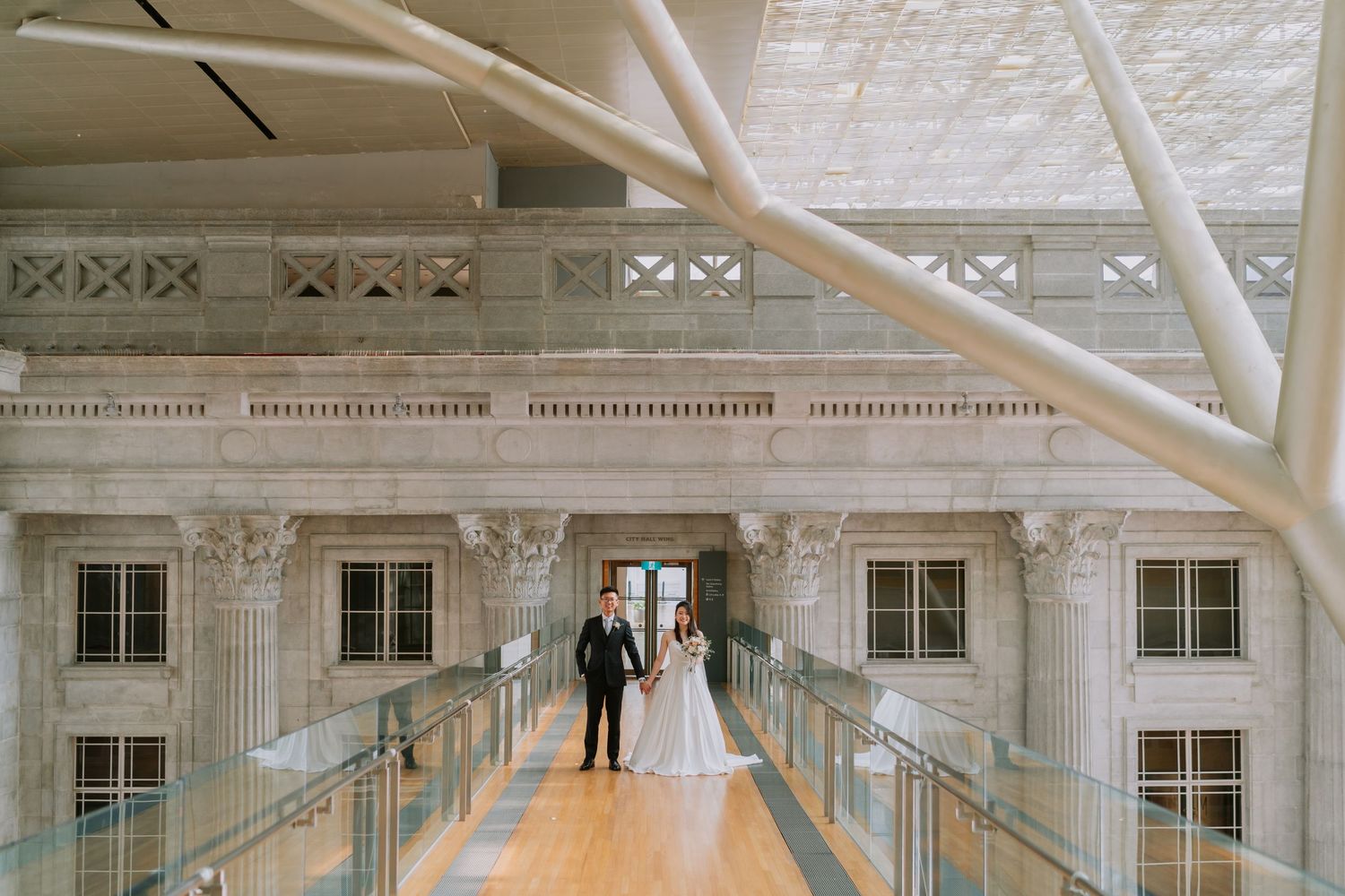 Bride and groom standing on a grand marble balcony inside a stunning heritage building.
