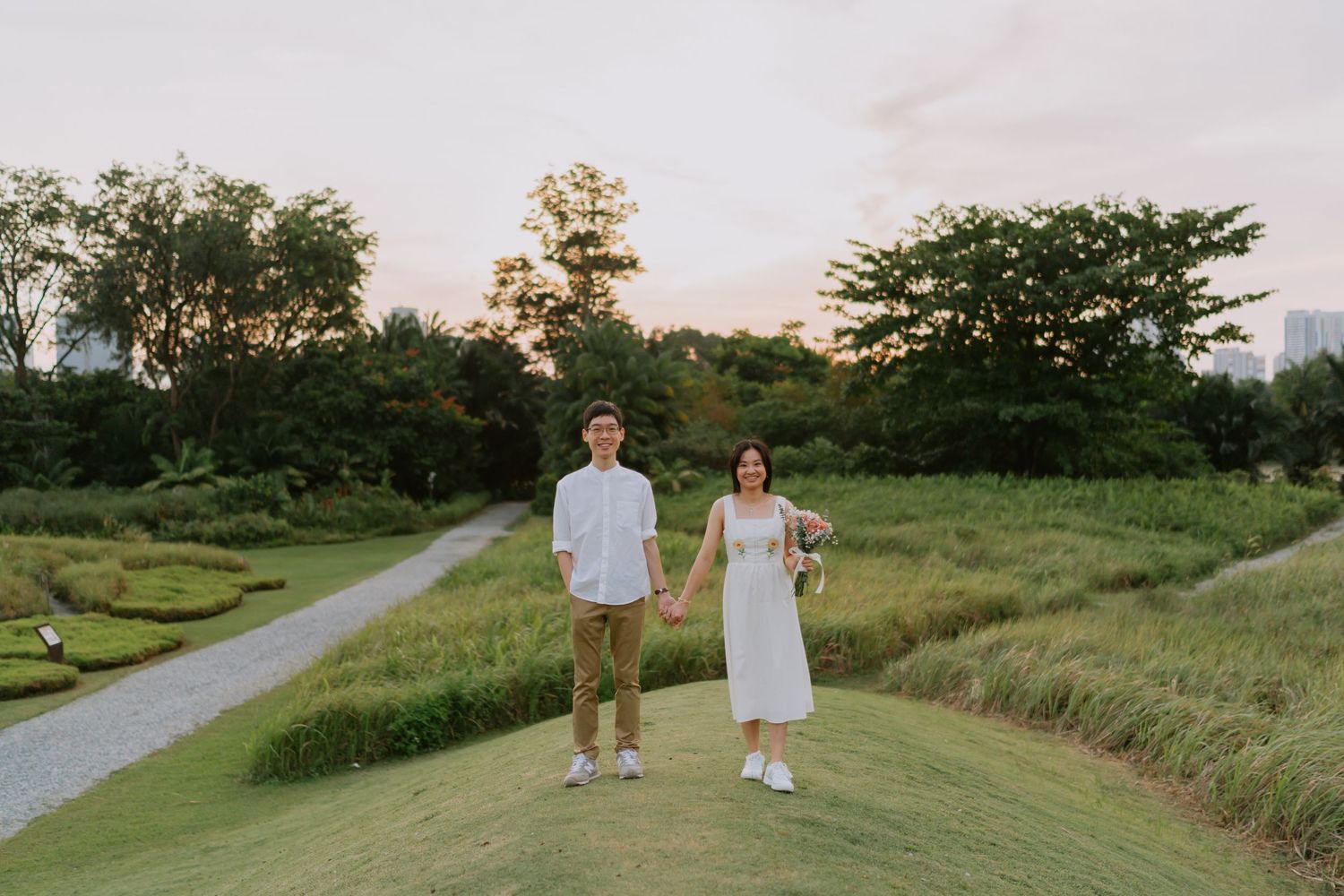 Couple holding hands while walking along a scenic garden pathway at golden hour sunset.