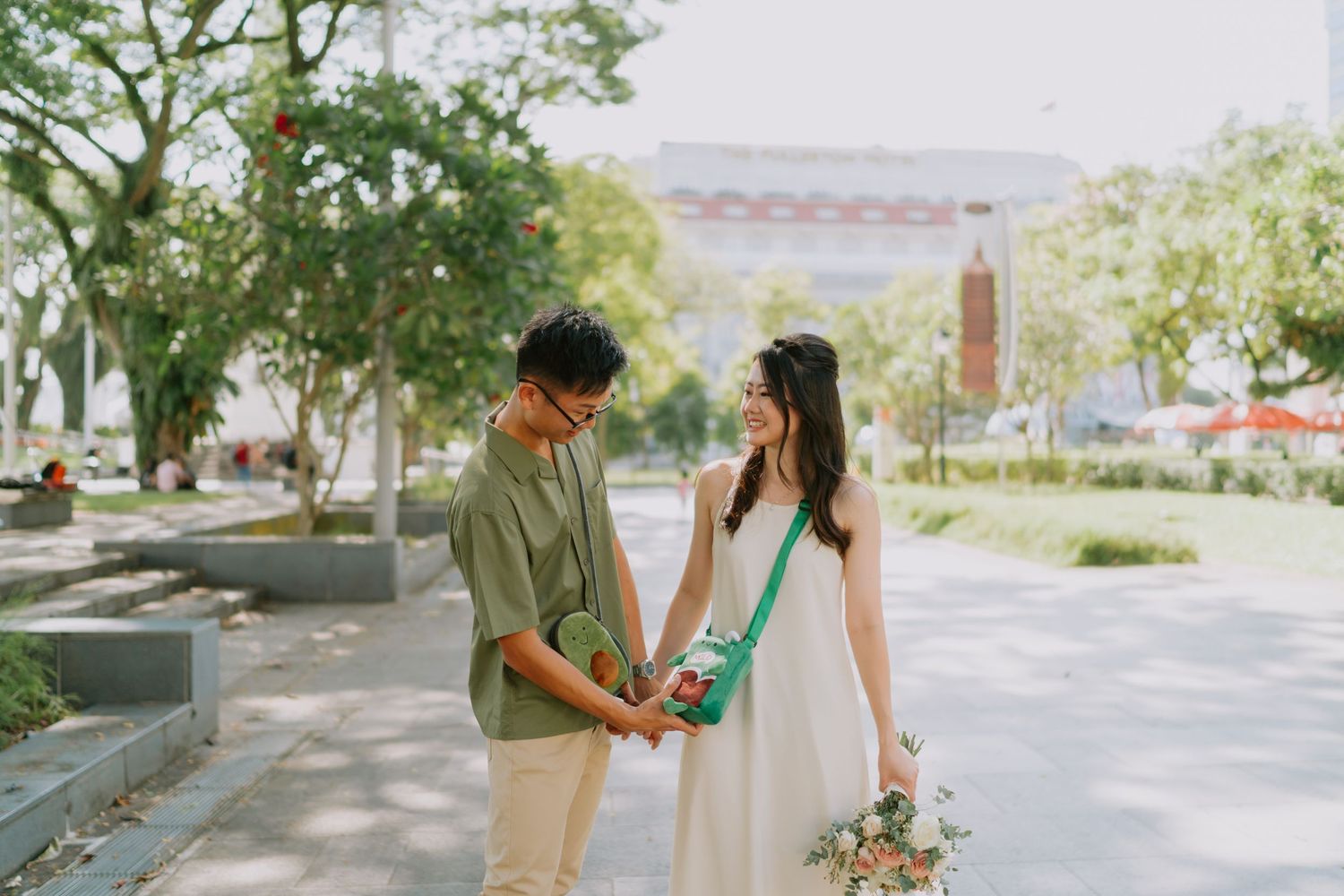 Couple walking hand in hand through sunny tree-lined park path in casual pre-wedding shoot.