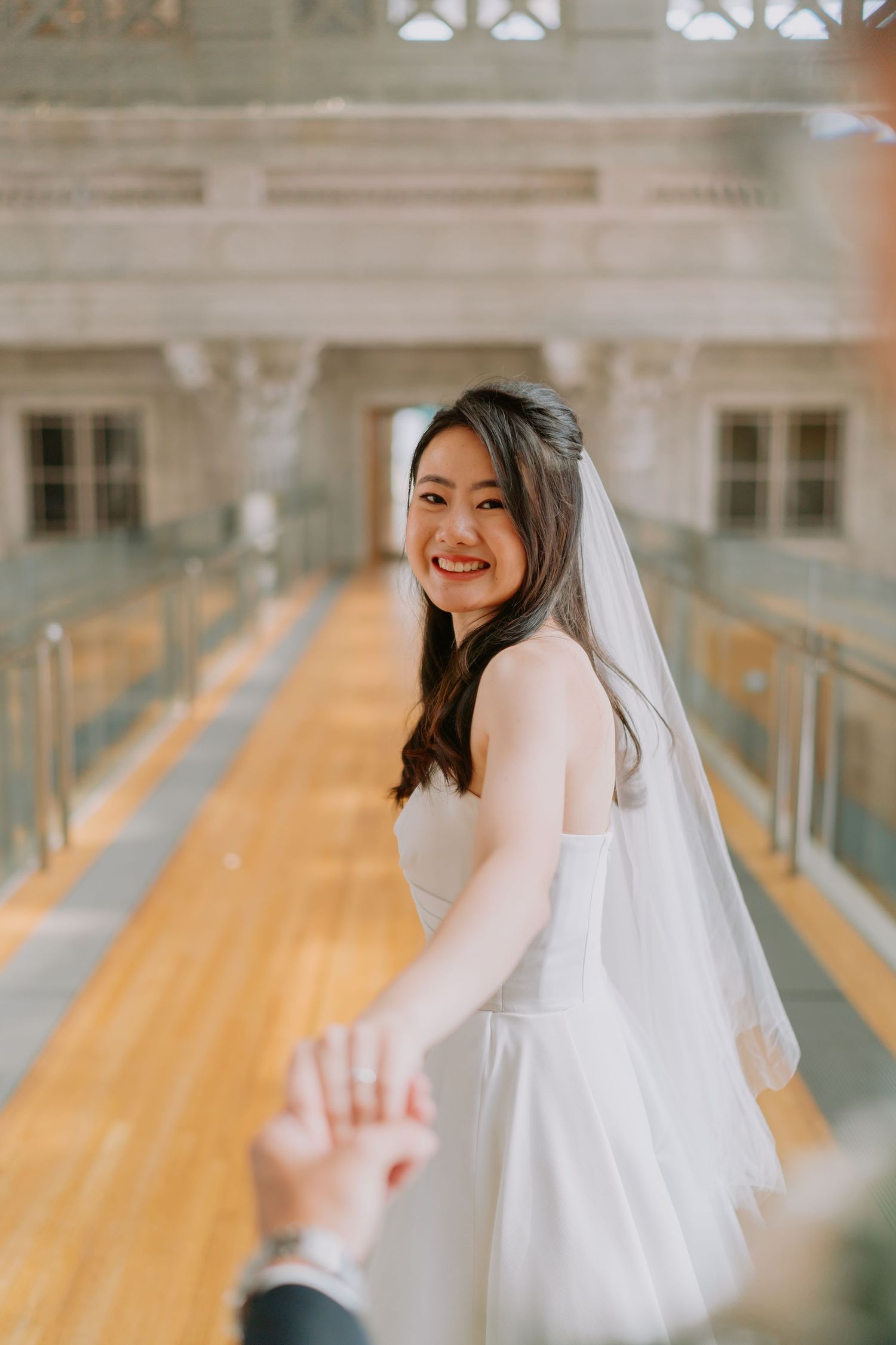 Radiant bride in a white gown and veil smiling while leading her groom by the hand.