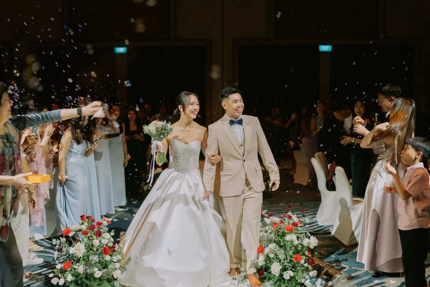 Bride and groom walk through confetti shower at elegant wedding reception with bridesmaids in blue dresses lining the aisle.