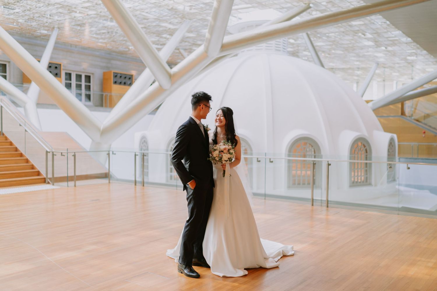 Asian wedding couple sharing romantic moment in stunning modern white domed venue with geometric structural details.