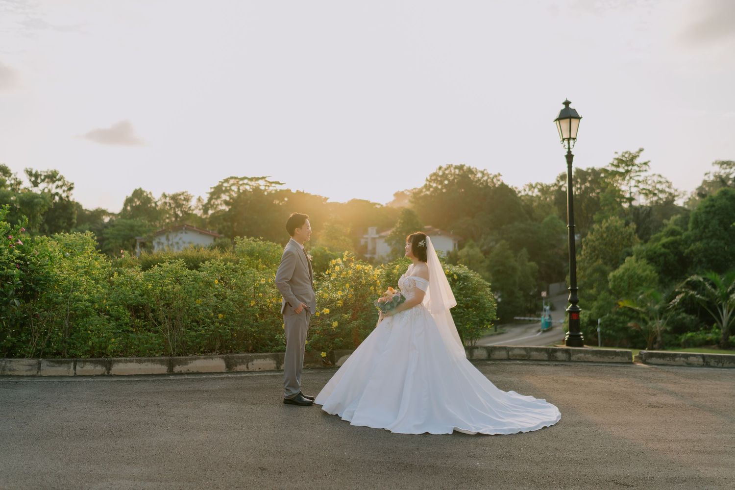 Bride and groom facing each other at sunset in lush garden, bride in flowing white ballgown.