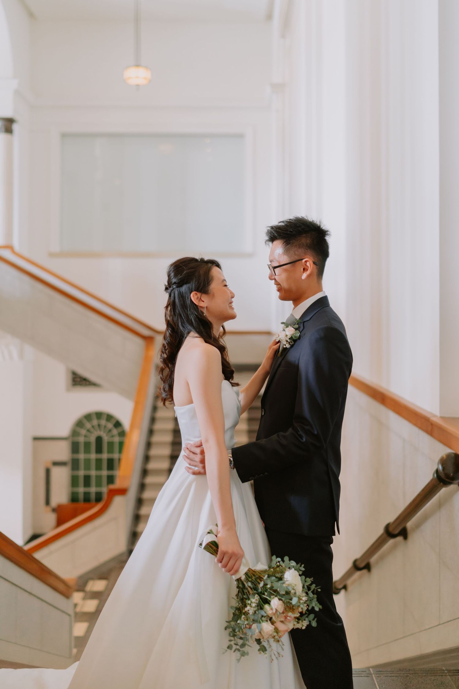 Bride and groom sharing an intimate moment on staircase, bride adjusting groom's suit lapel.