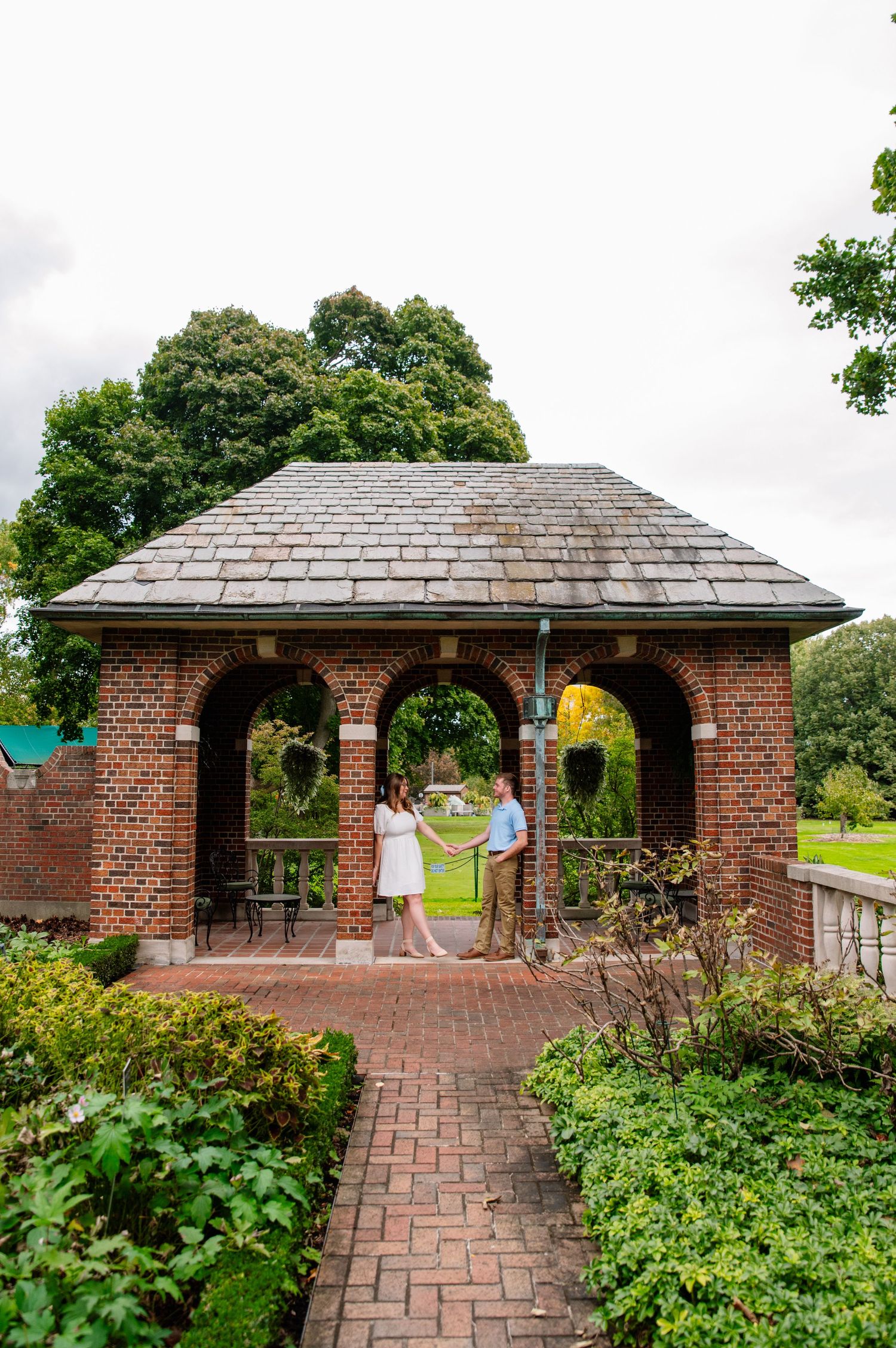 Couple poses in brick gazebo surrounded by beautiful landscaped gardens.
