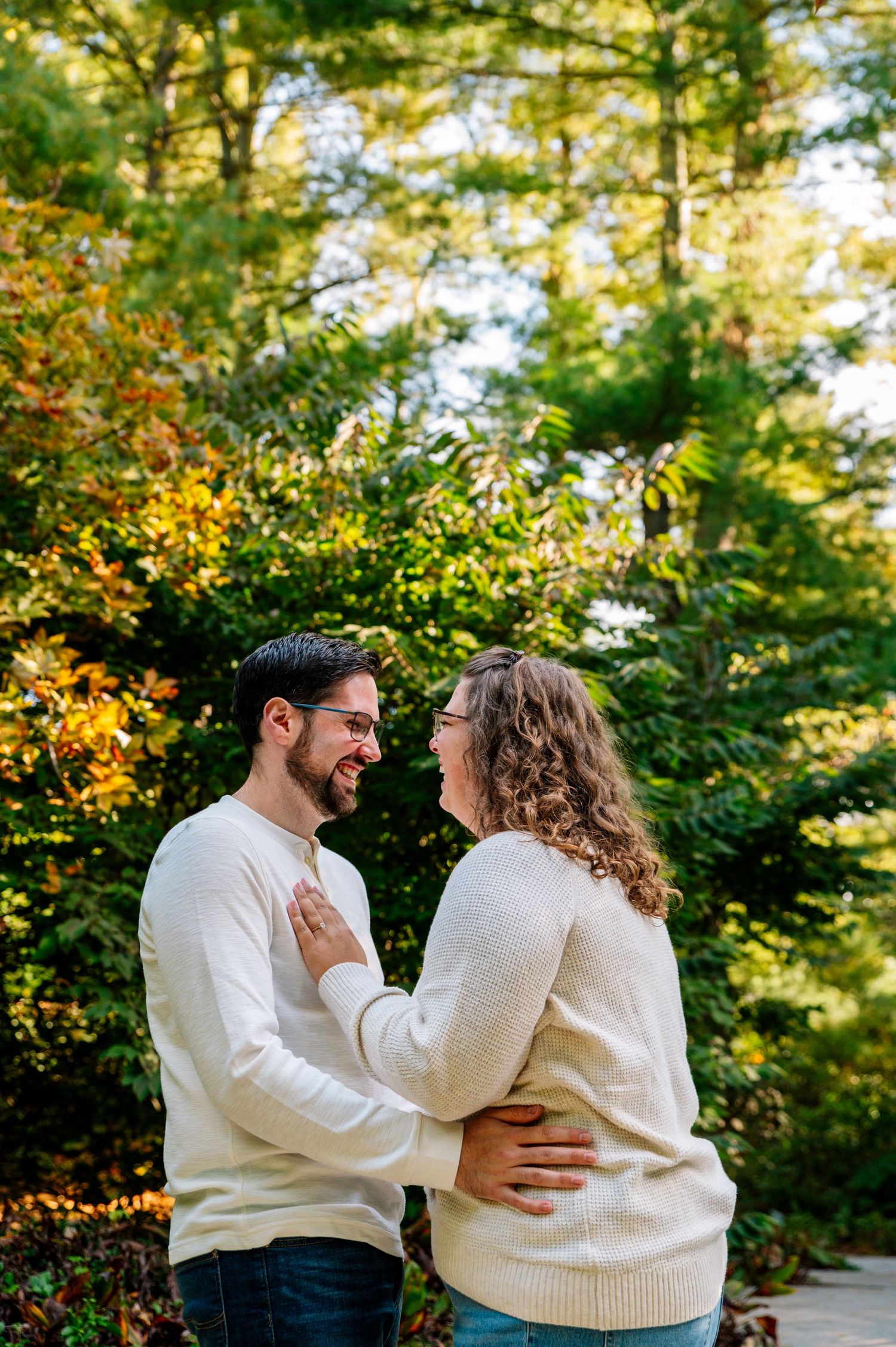 A couple in matching cream sweaters share an intimate moment surrounded by autumn foliage.