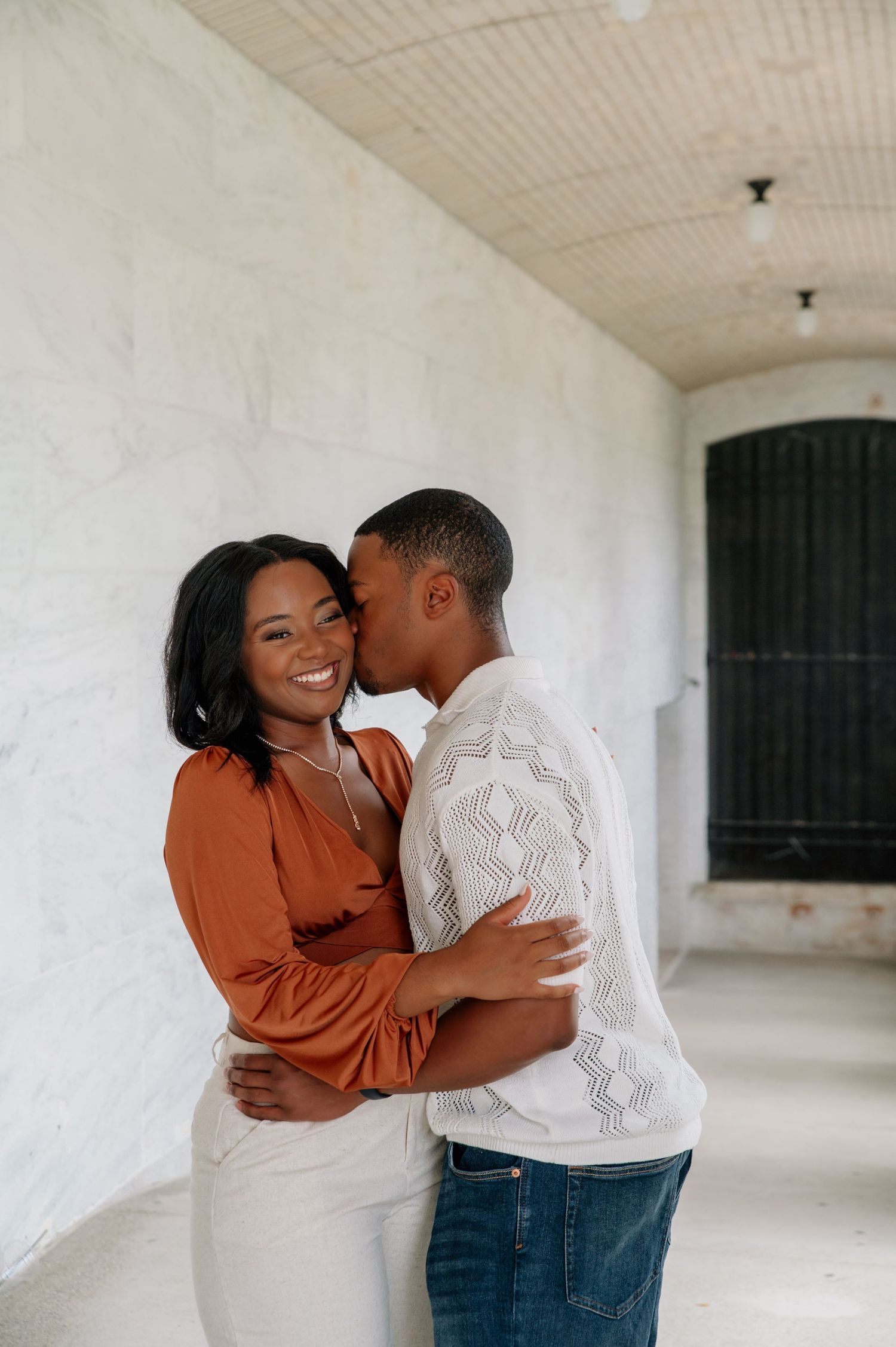 Romantic couple sharing an intimate moment against a white wall.