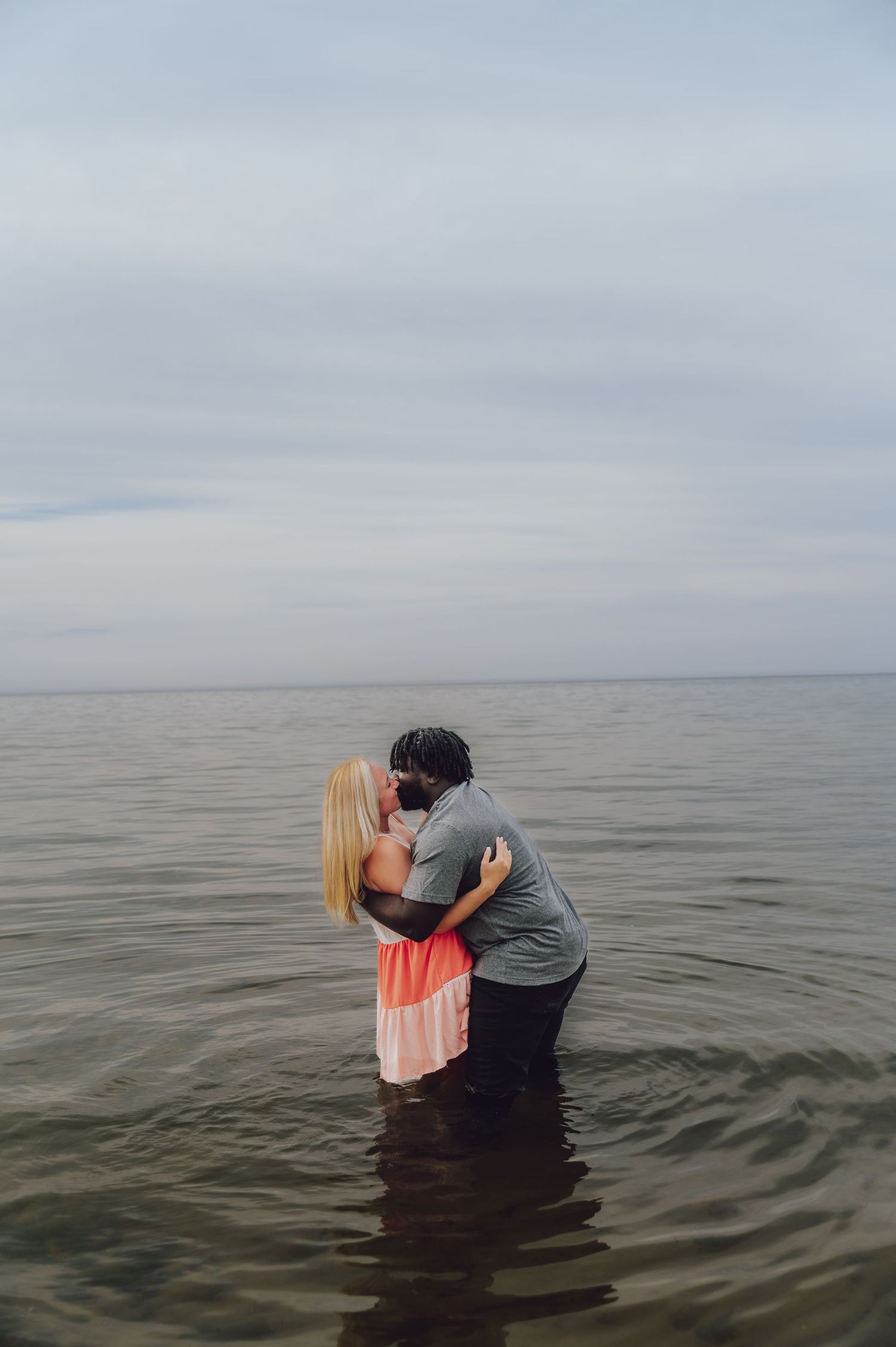 Couple embracing while standing in water against a cloudy sky backdrop.
