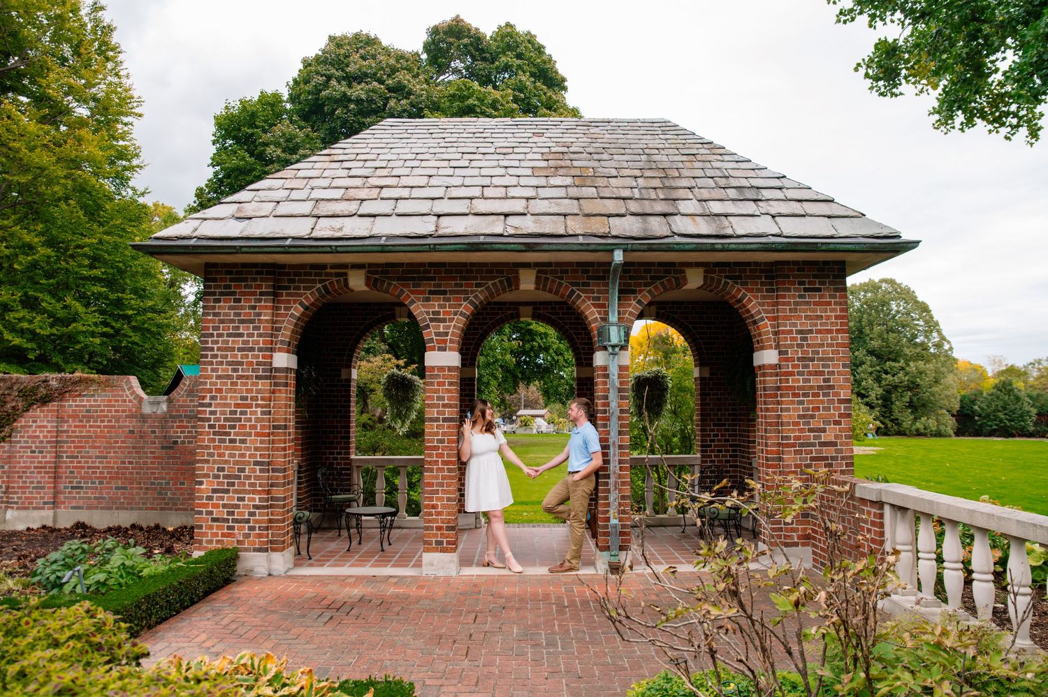A brick gazebo with arched openings nestled in a lush garden setting during a spring day.