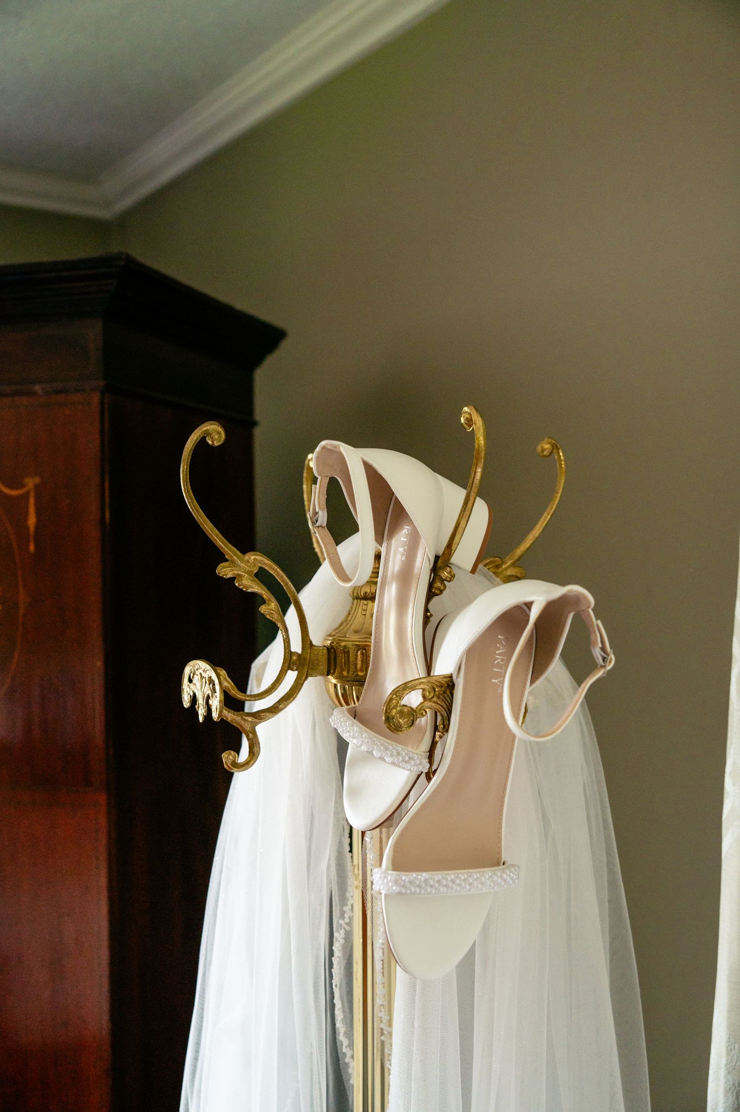White gowns hang elegantly from ornate gold clothing hooks mounted on a dark wood wall in a dressing room.