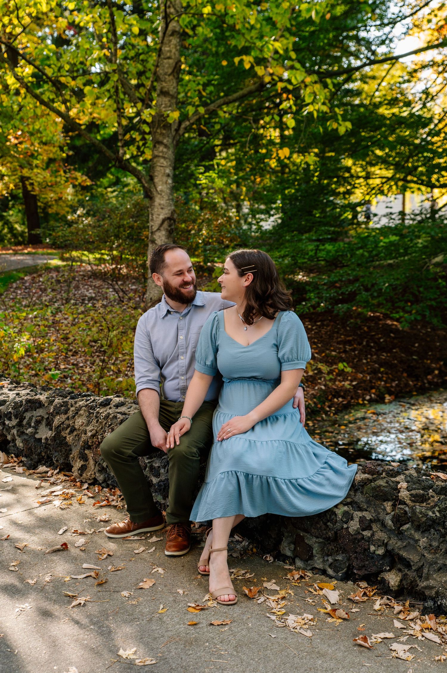 Couple sitting on stone wall enjoying playful moment in autumn garden setting.
