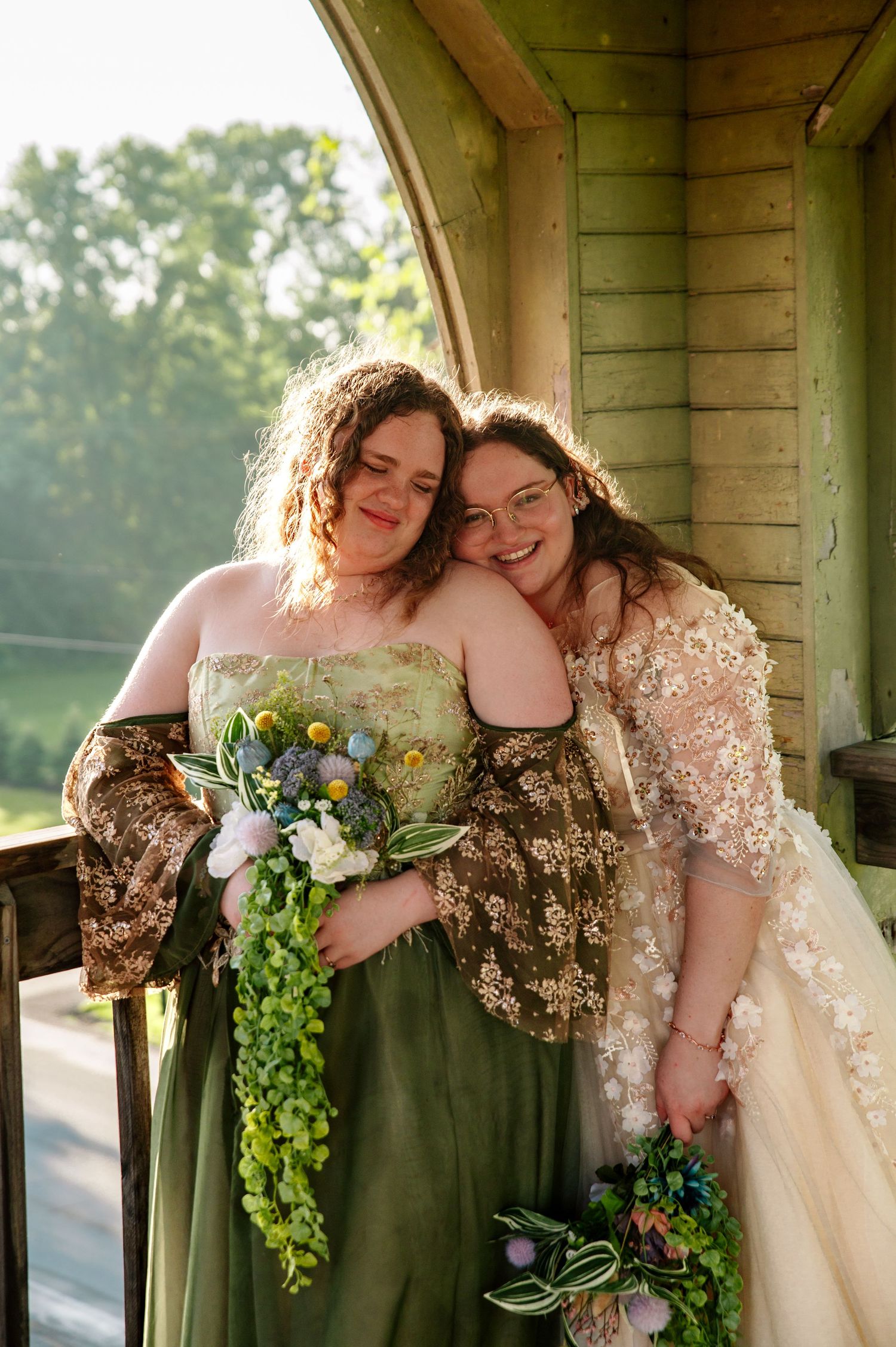 Two people in wedding attire share intimate moments in a rustic wooden gazebo with greenery and flowers.