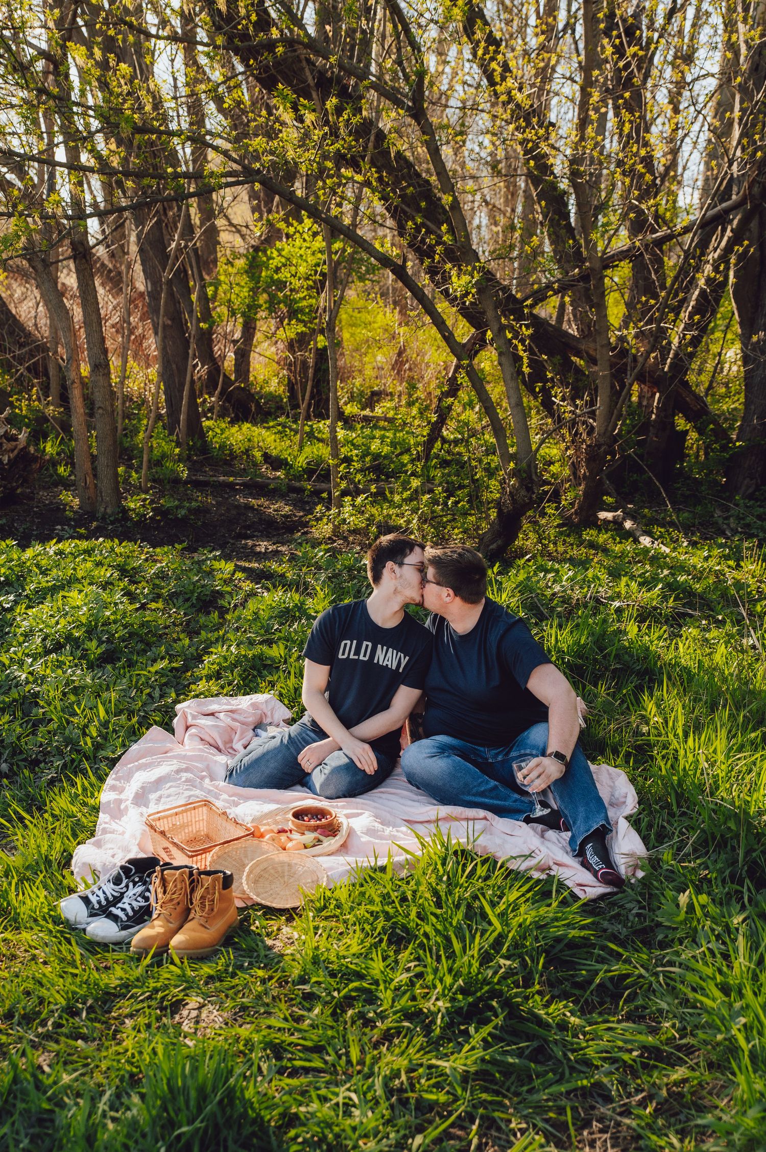 A picnic scene on a blanket surrounded by spring greenery and budding trees.