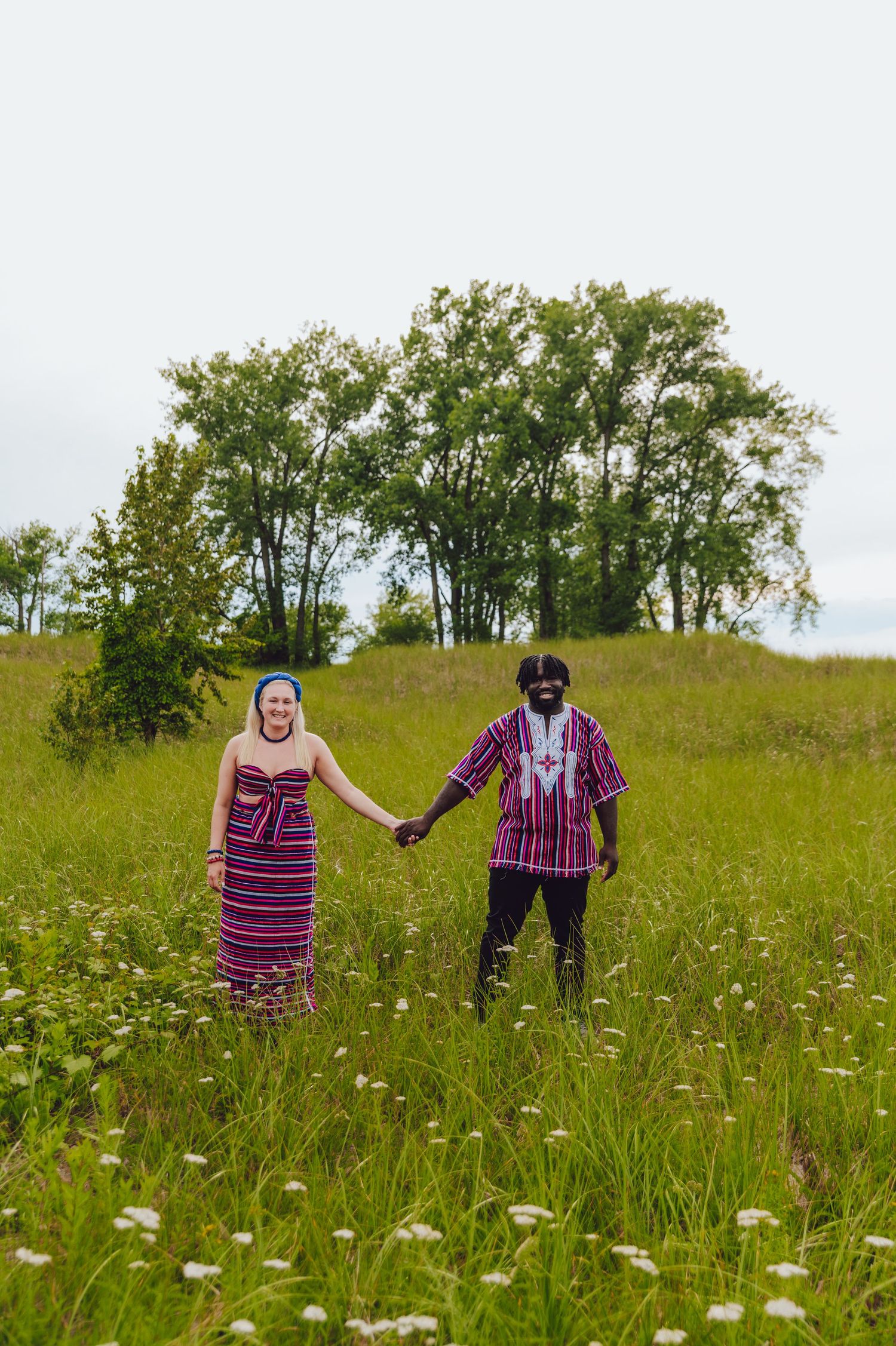 Couple holding hands while standing in a wildflower meadow wearing coordinated striped attire.
