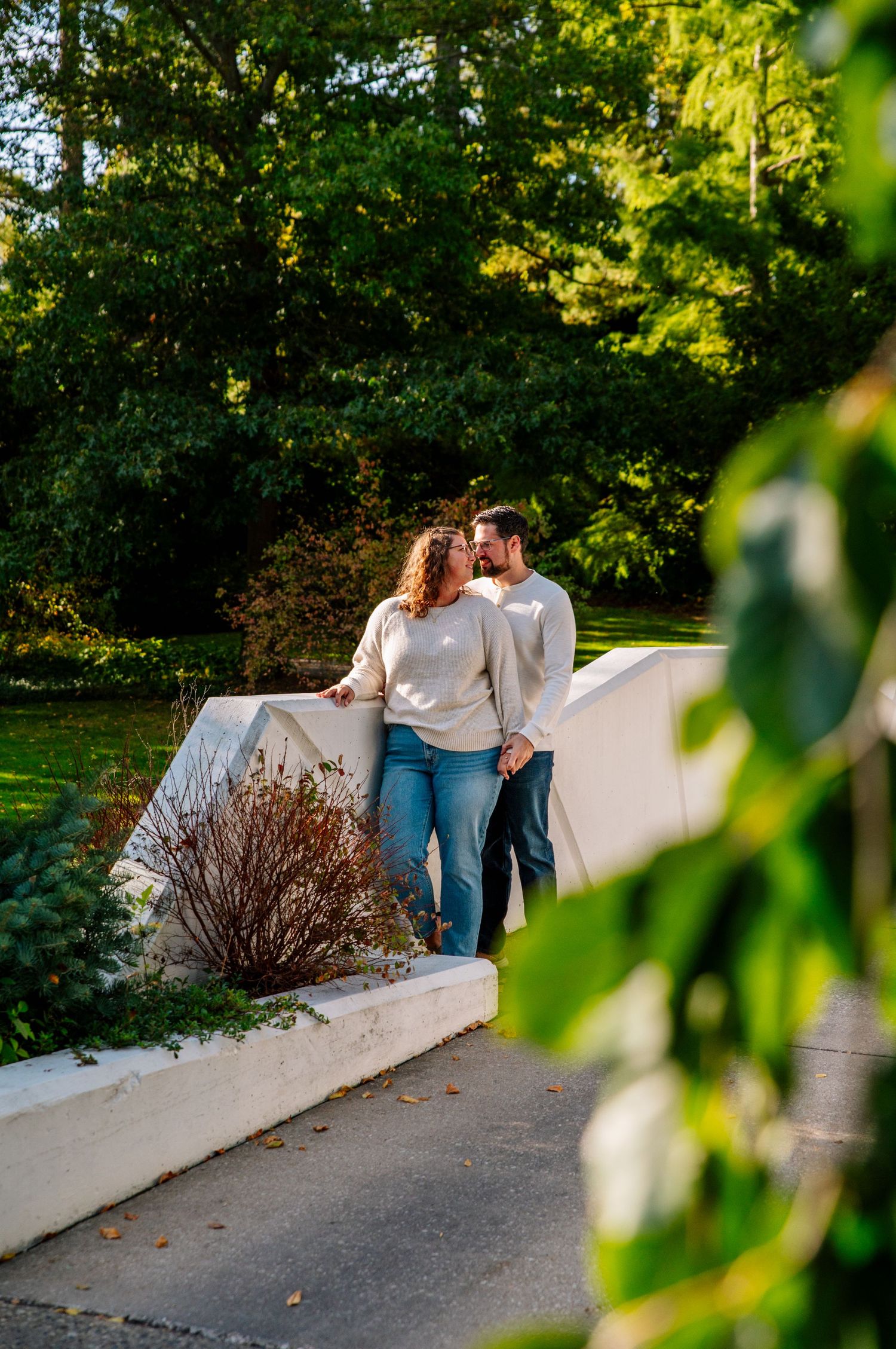 A couple in casual attire shares an intimate moment on a white wall in a garden setting.