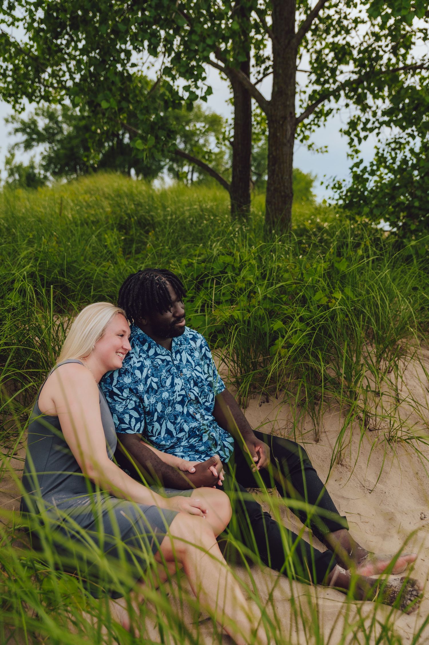 Couple relaxing together on a sandy beach nestled among tall grass.