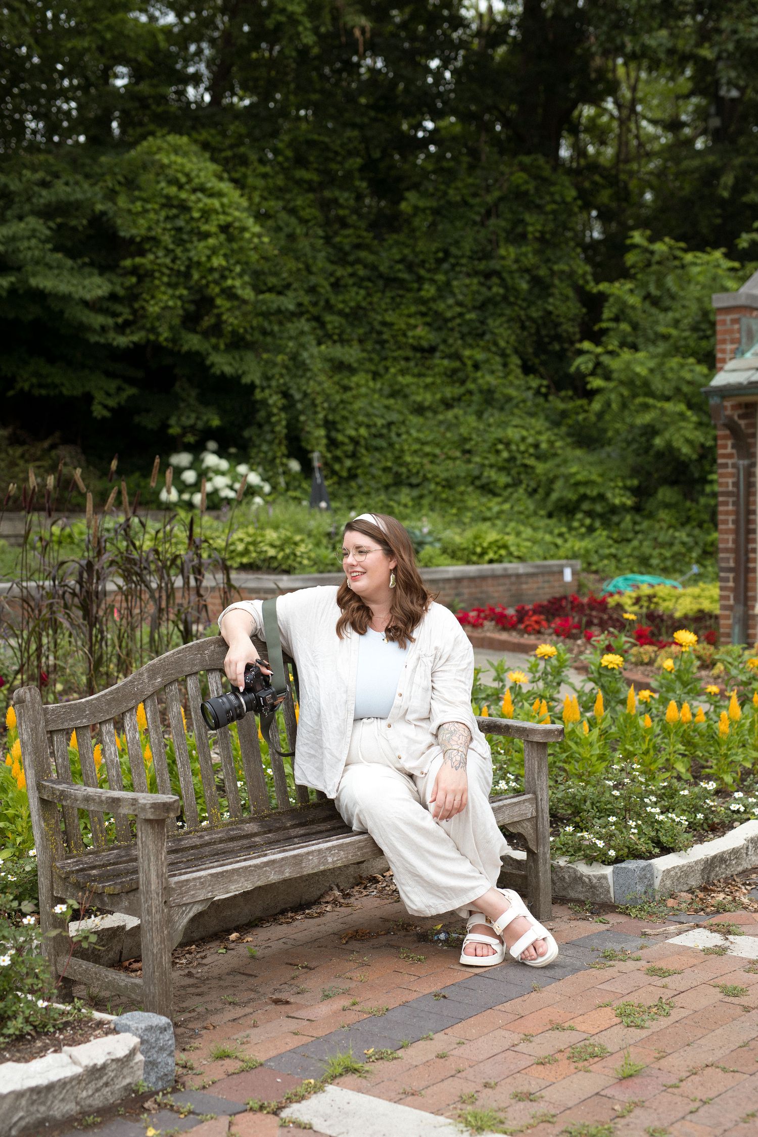Person in white outfit lounging on wooden garden bench surrounded by blooming flowers.