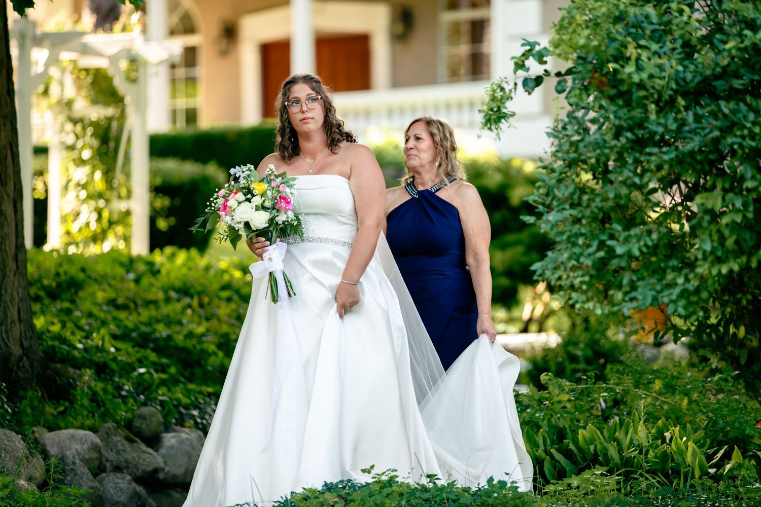 Three elegantly dressed people pose together on a lush garden path during a formal outdoor event.