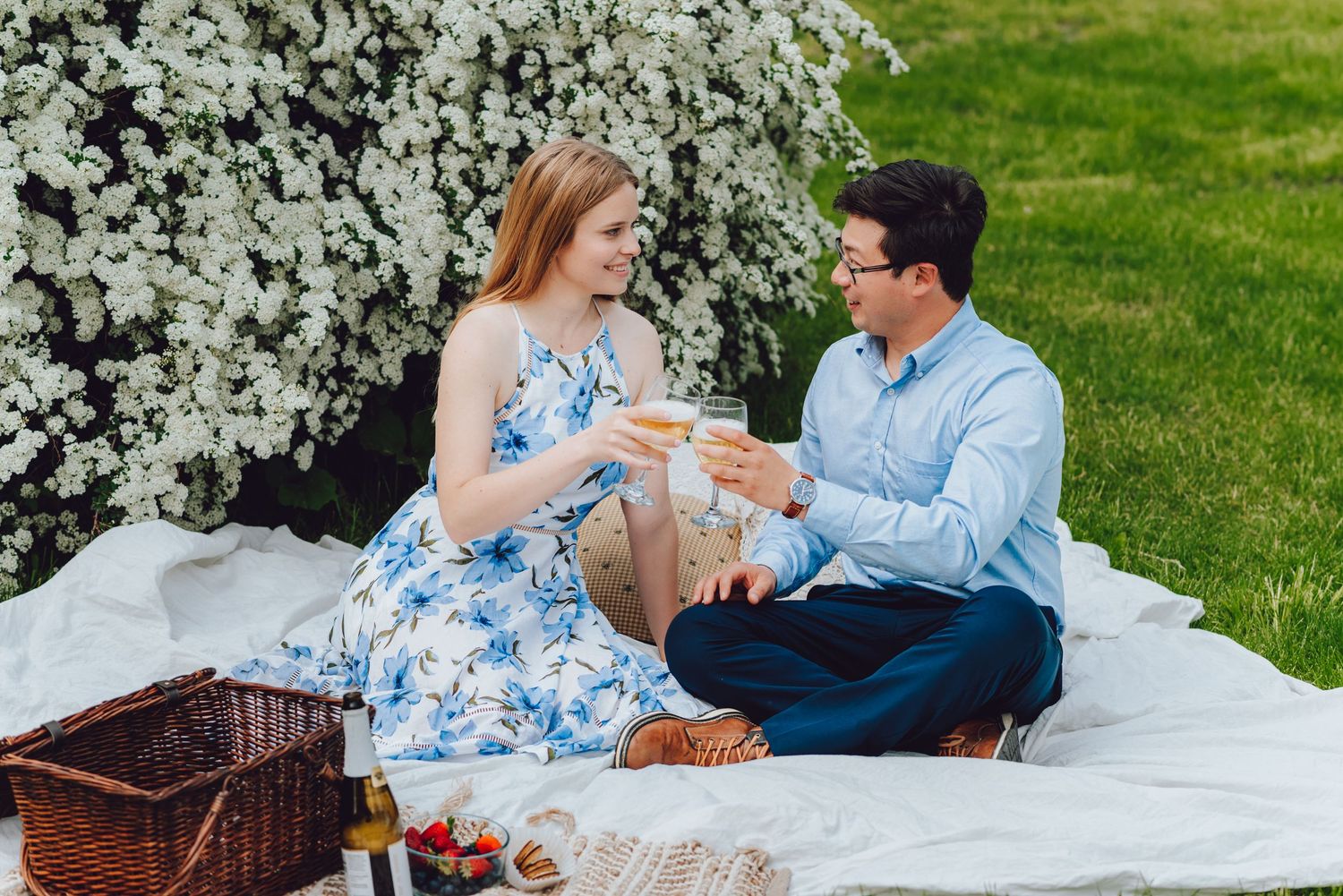 A spring picnic setup with a wicker basket and blanket under blooming white flowers.