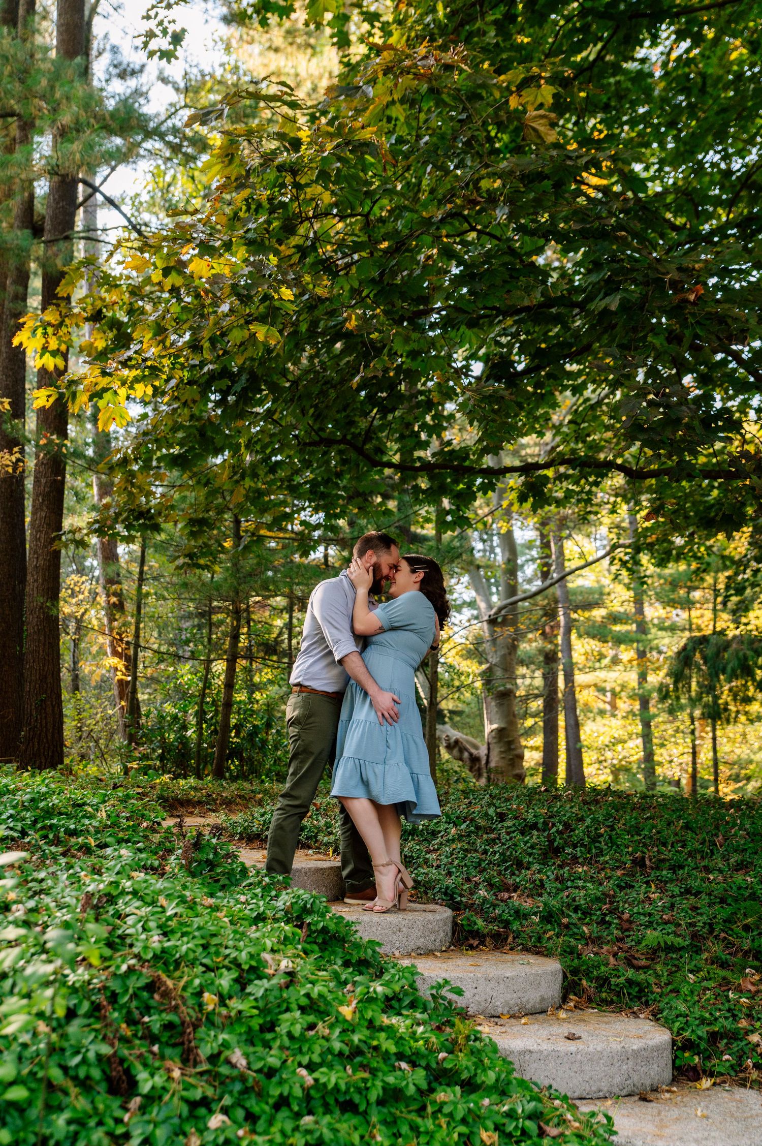 Tender embrace on stone steps amid verdant garden landscape in golden hour light.
