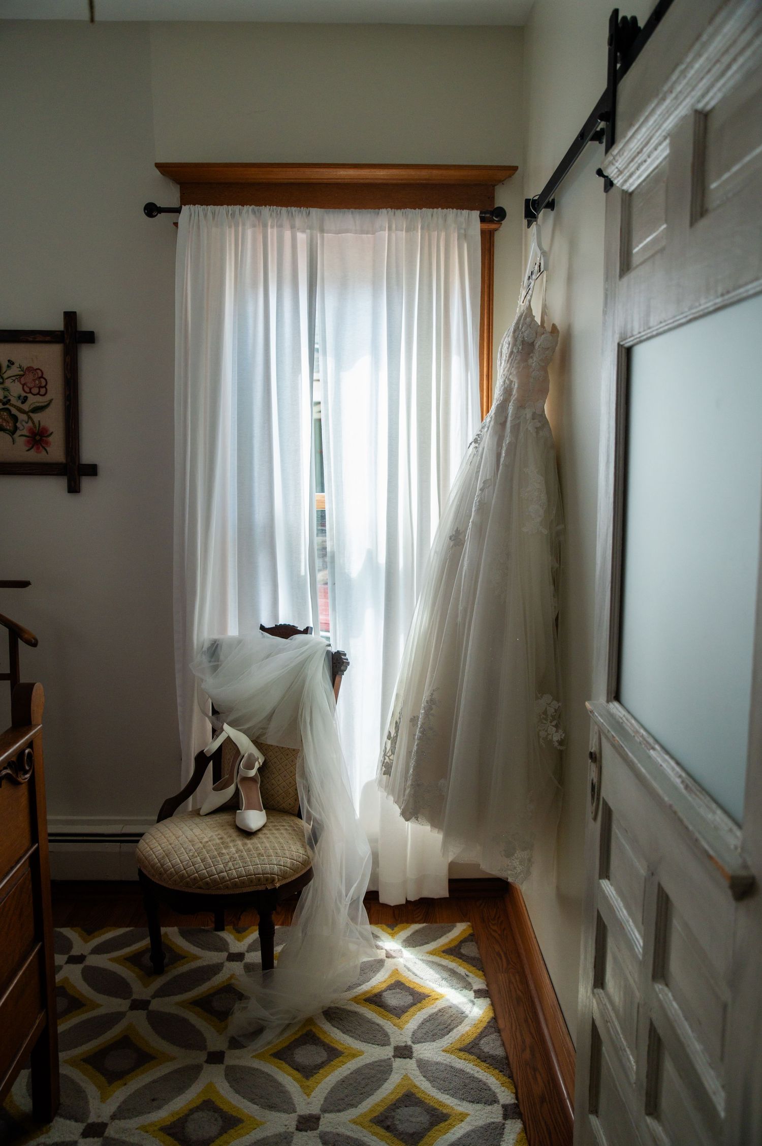 White sheer curtains billow in a window with natural sunlight streaming through in a room with geometric patterned carpet.