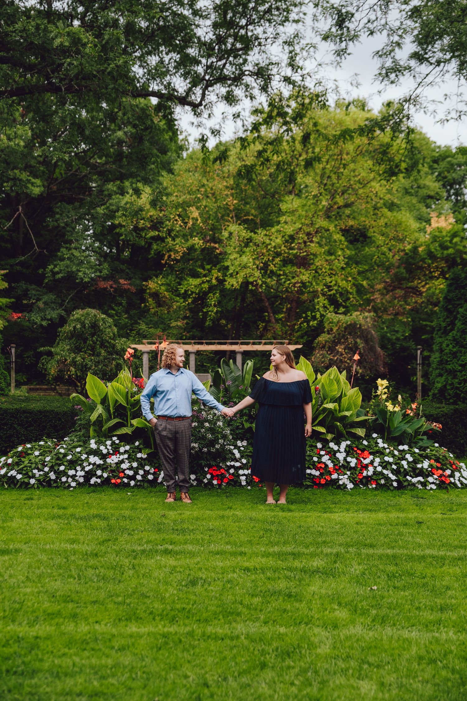 Couple standing together on manicured lawn with floral garden border.
