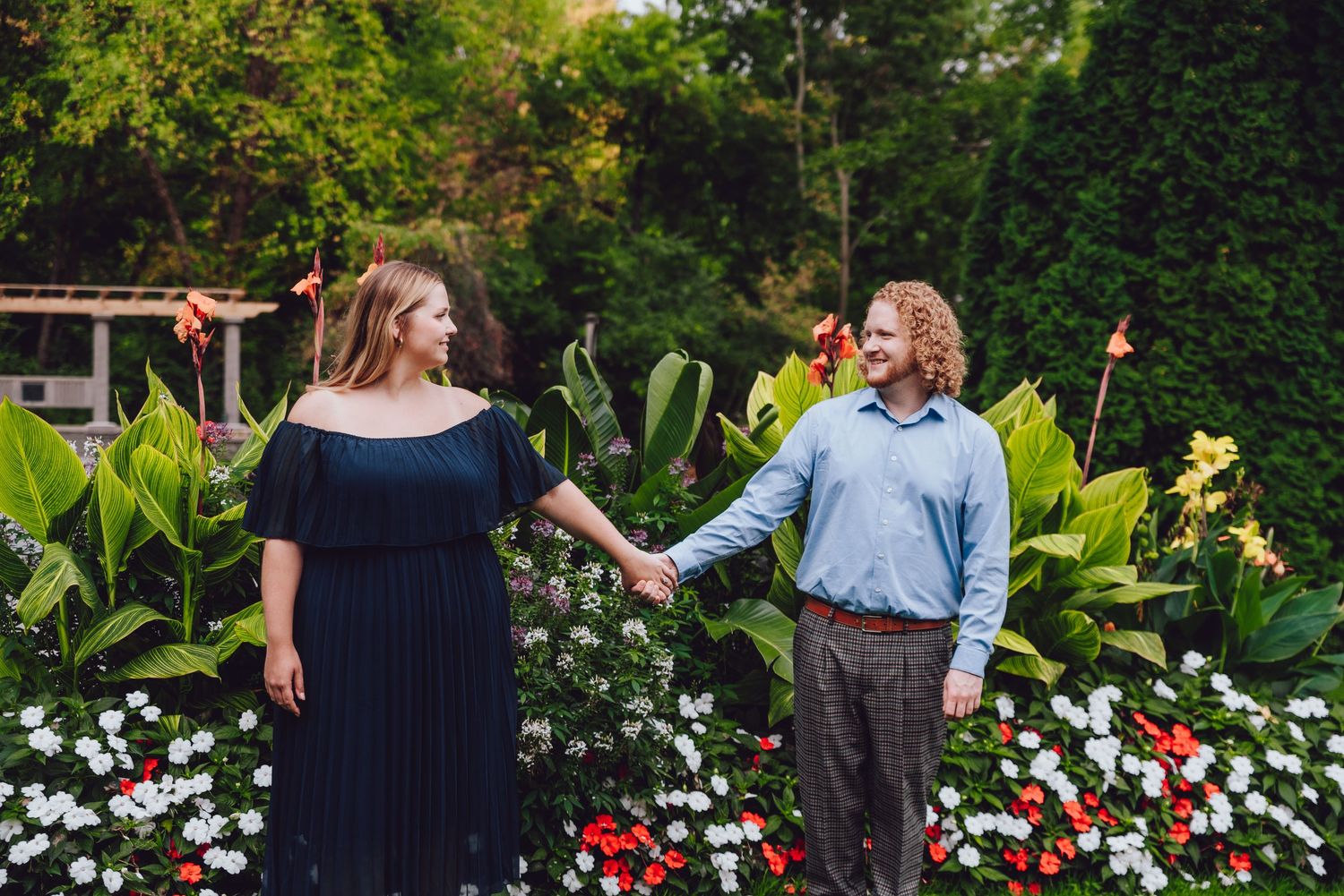 Couple holding hands in garden with colorful flower beds and greenery.