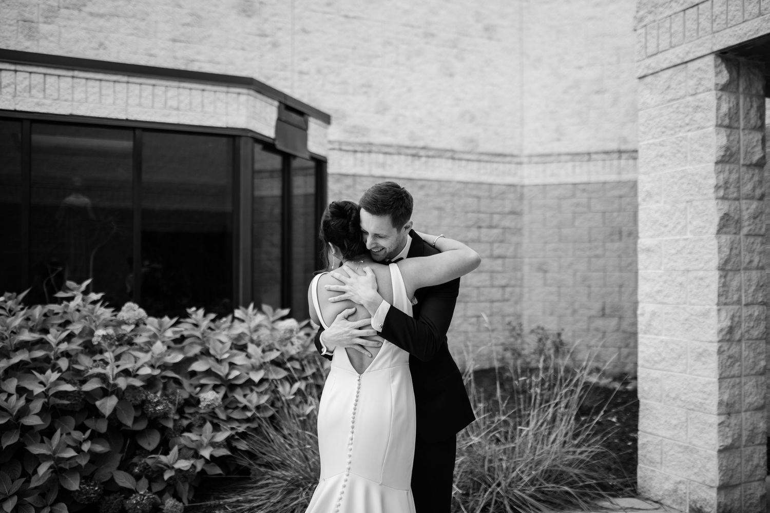 A couple shares a romantic moment during their wedding celebration outside a stone building.